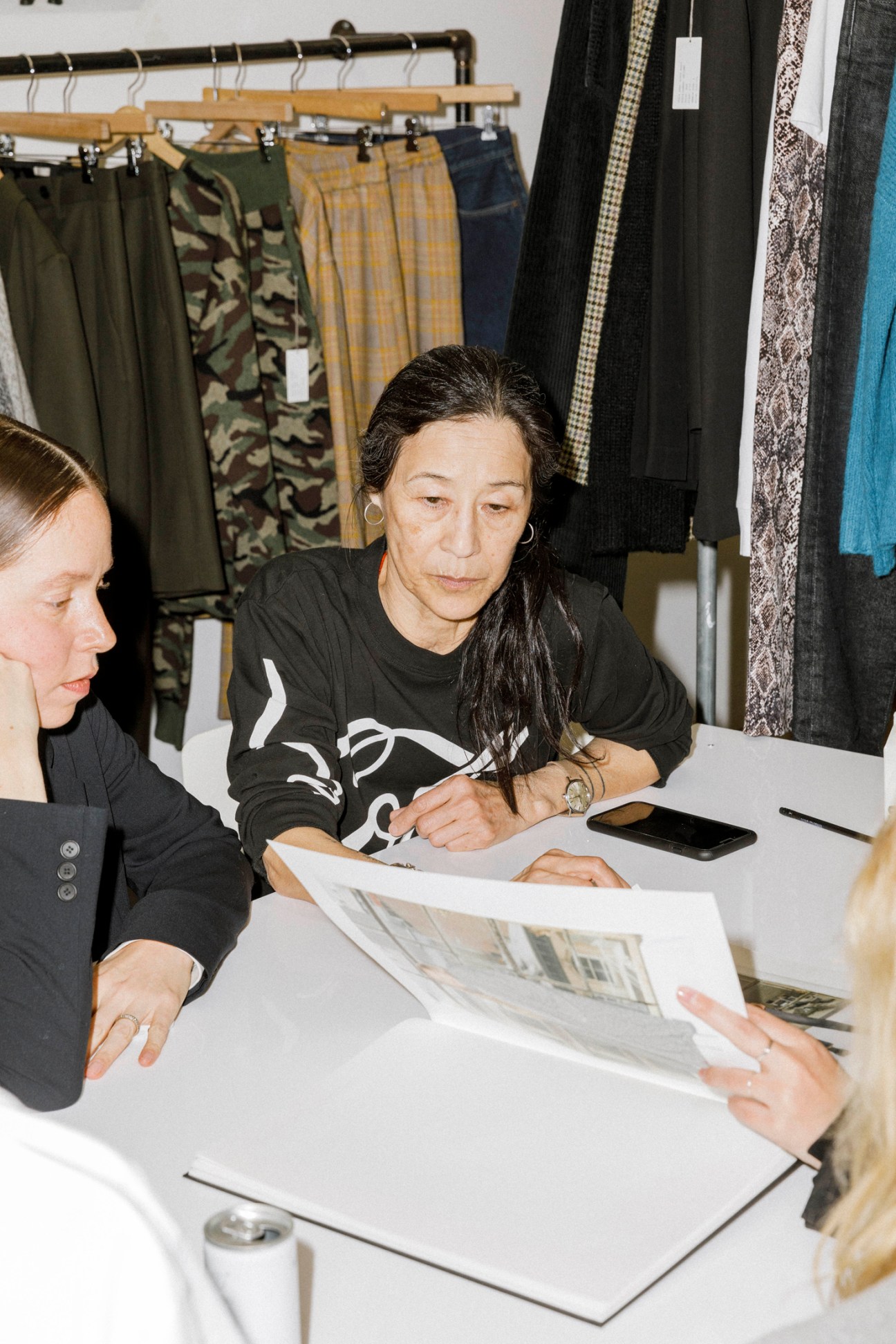 Stella Ishii sits at a white table reviewing documents with two other people in her fashion showroom