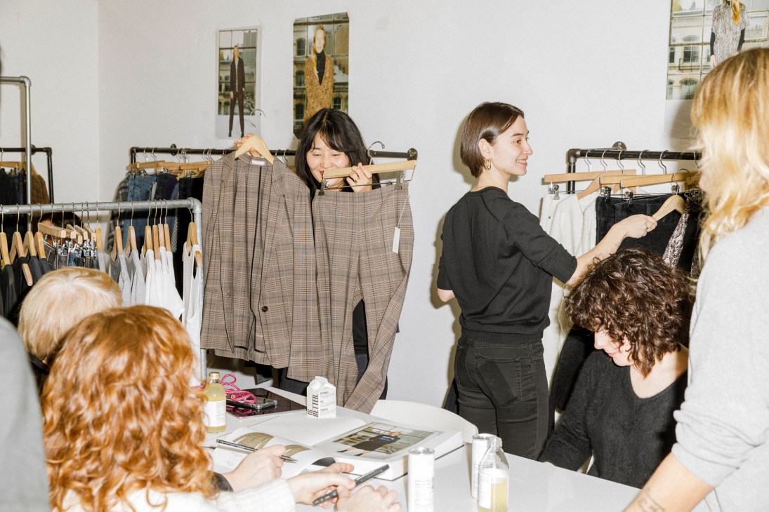 Fashion professionals examining clothing on racks and discussing items around a white table in a showroom setting