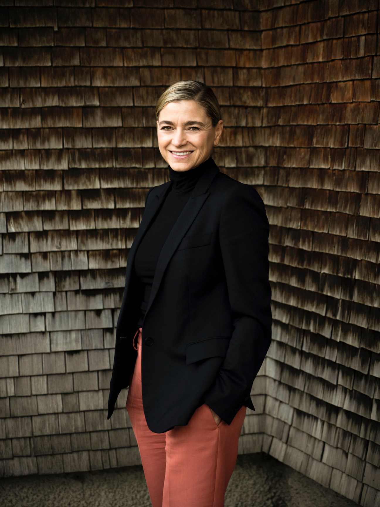 Susanne Kaufmann, founder of the cosmetics brand, smiling against a wooden shingle wall.