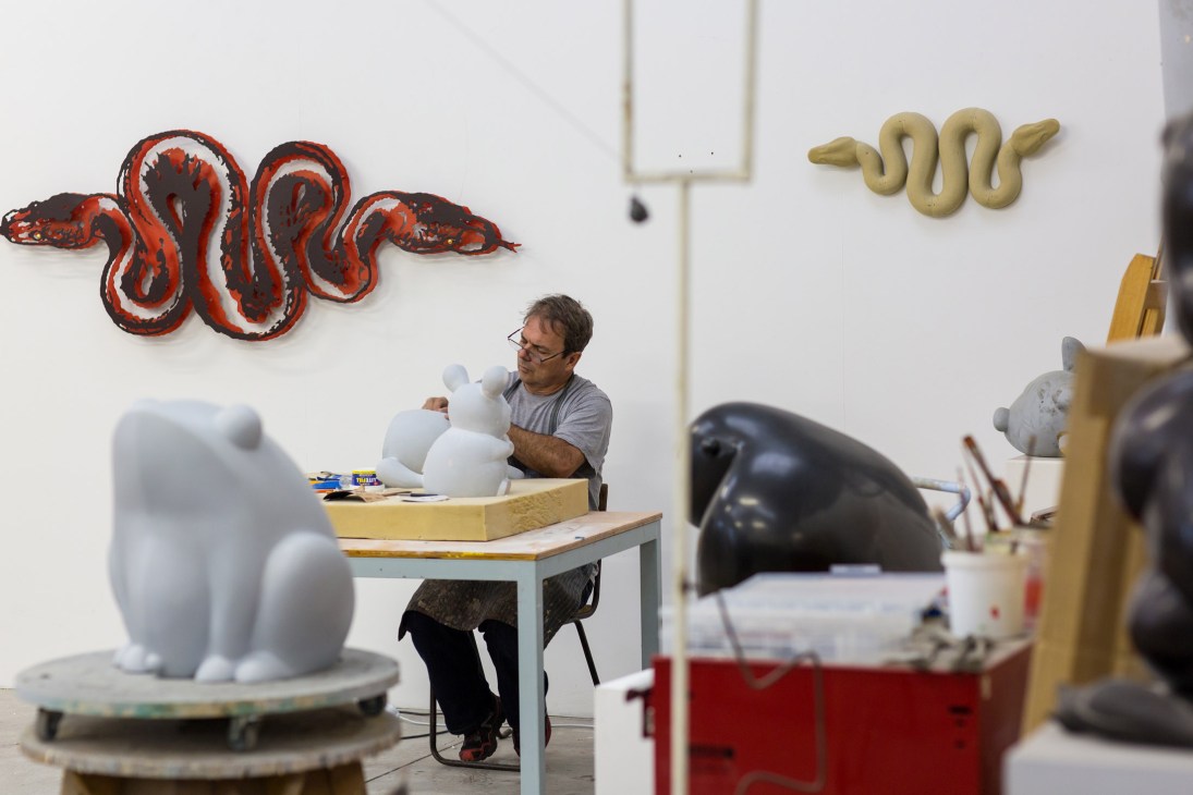 Artist Brett Murray working in his studio surrounded by sculptural works including white forms and a red snake sculpture on the wall.