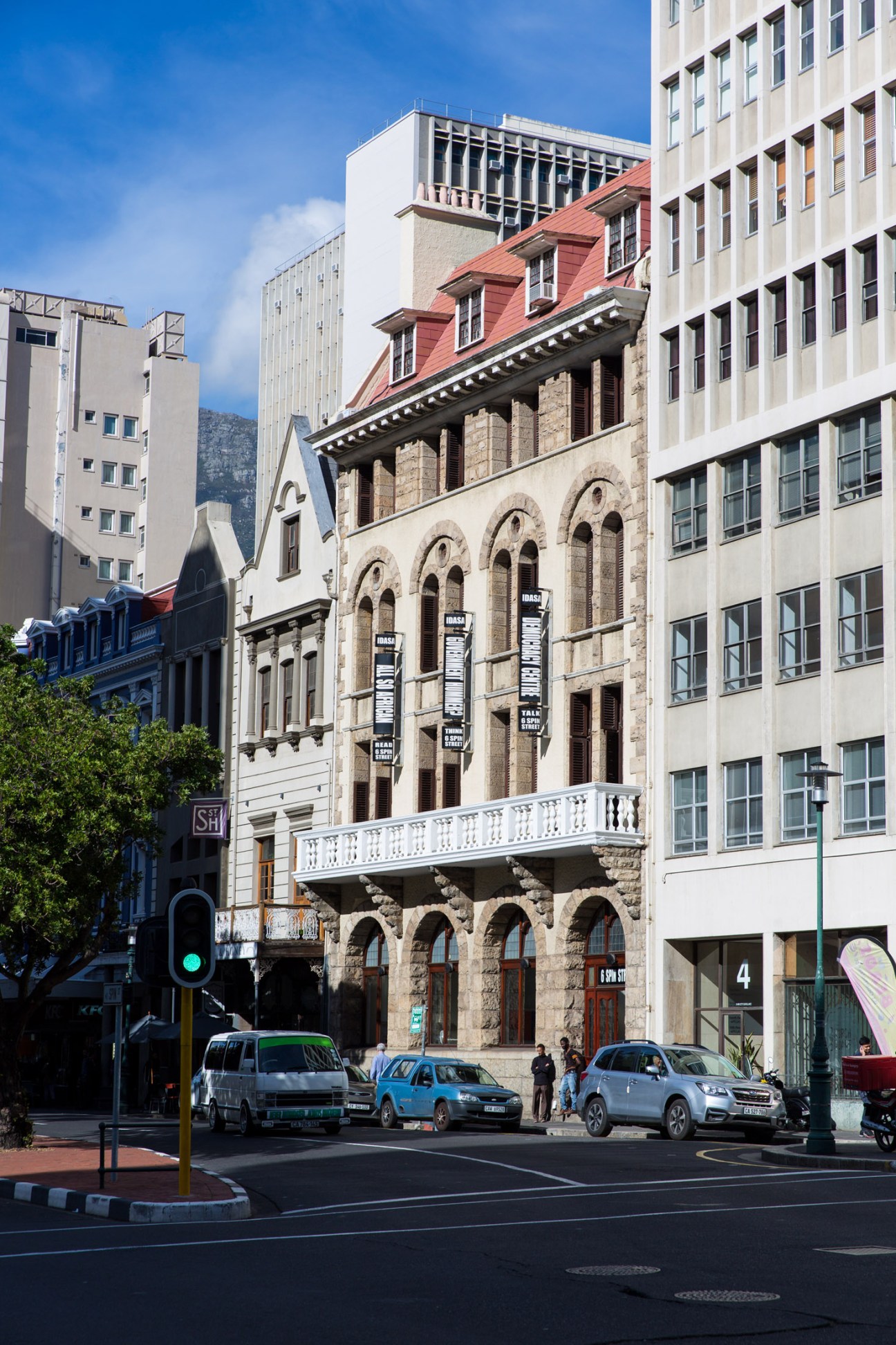 Historic stone building with red roof and arched windows displaying gallery banners on a Cape Town street.