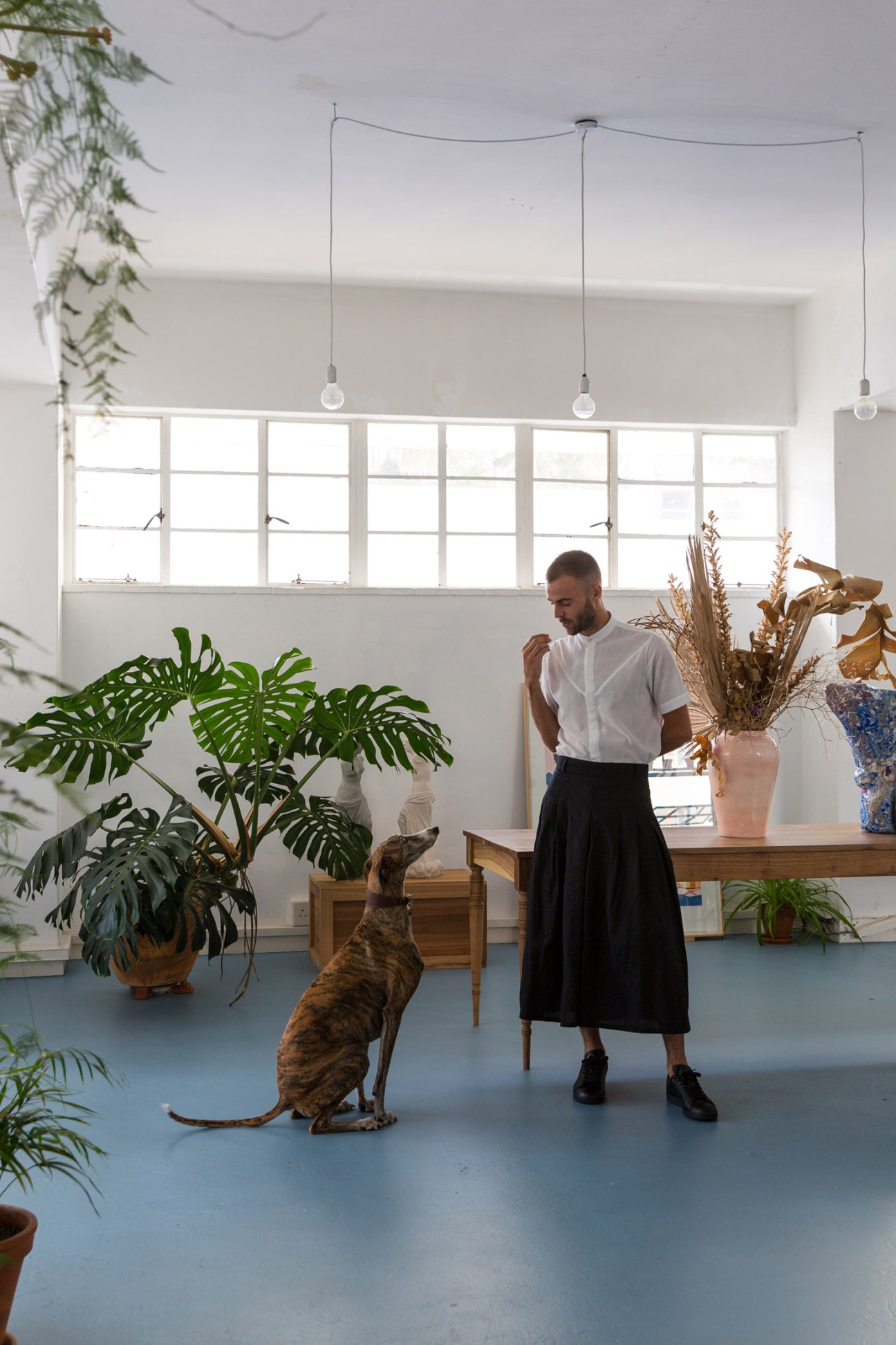 Artist Morné Visagie and his dog Tracer in a bright studio space with plants and pendant lights.