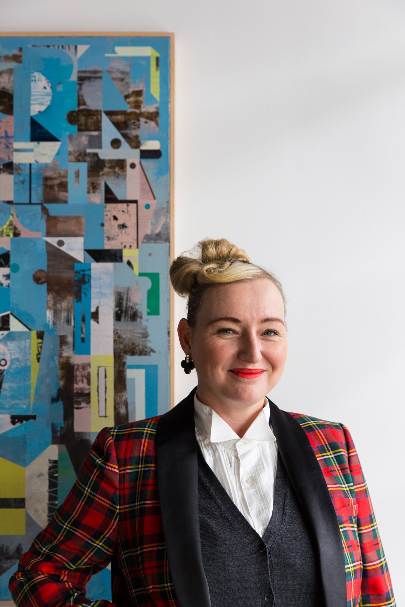 Curator Ashleigh McLean stands in front of an abstract collage artwork with blue, geometric shapes and photographic elements.