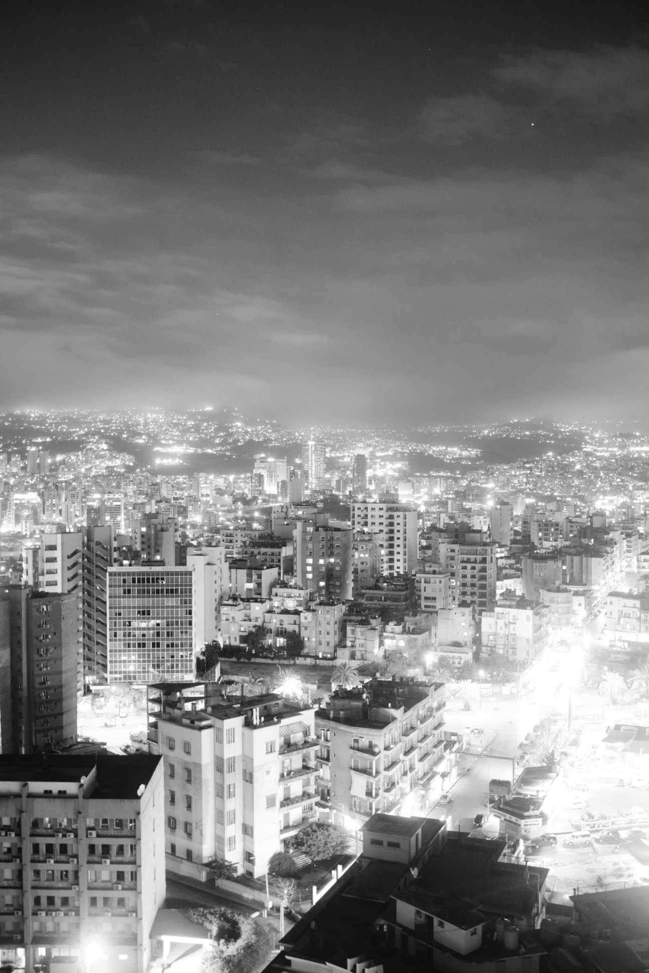 Black and white nighttime cityscape of Beirut with illuminated buildings and streets stretching to the horizon.