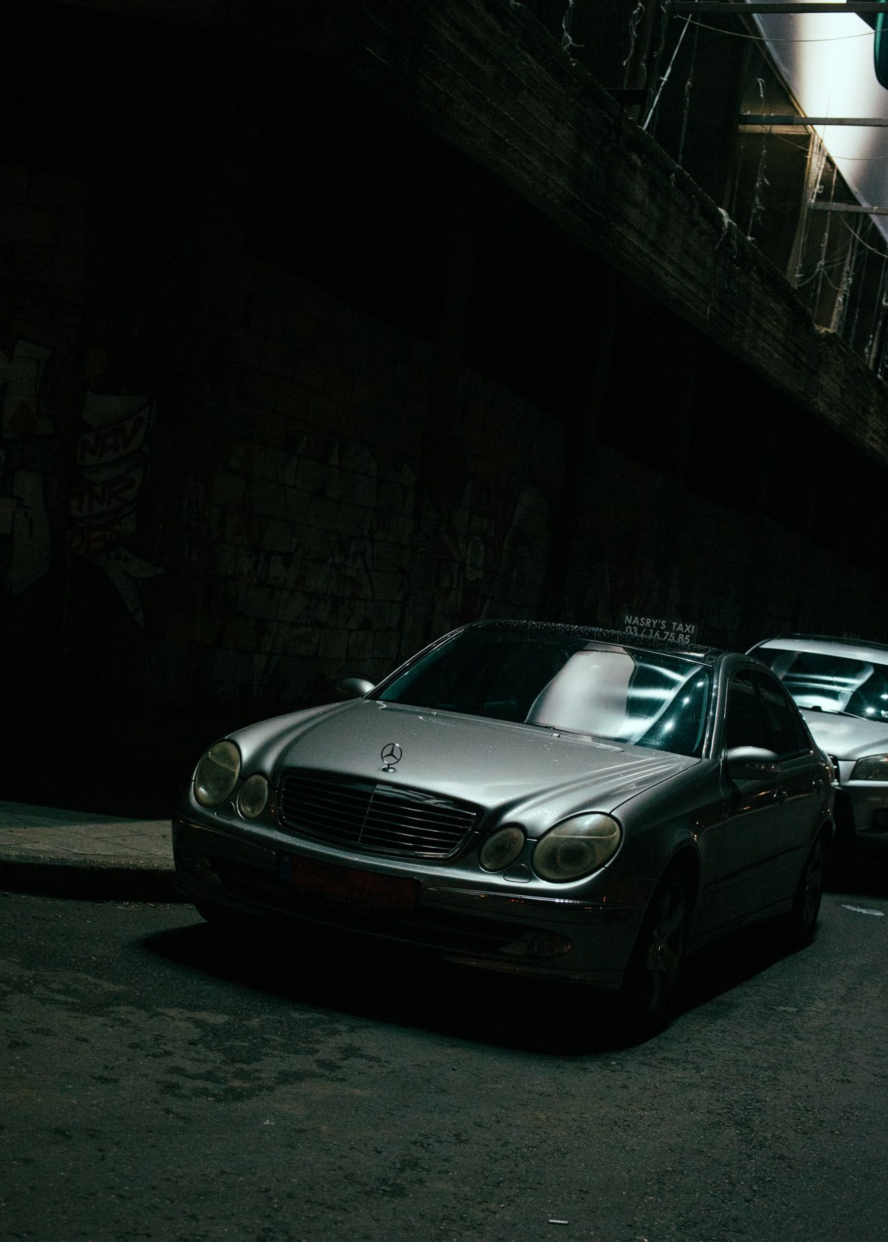 A silver Mercedes taxi parked on a dark Beirut street at night.