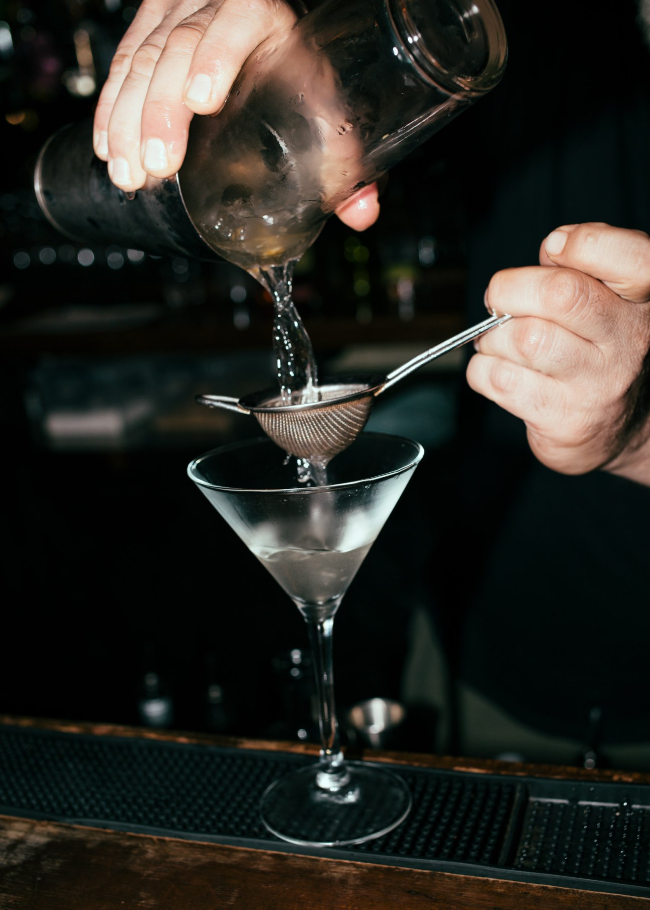 Bartender pouring a cocktail through a strainer into a martini glass at a Beirut bar.