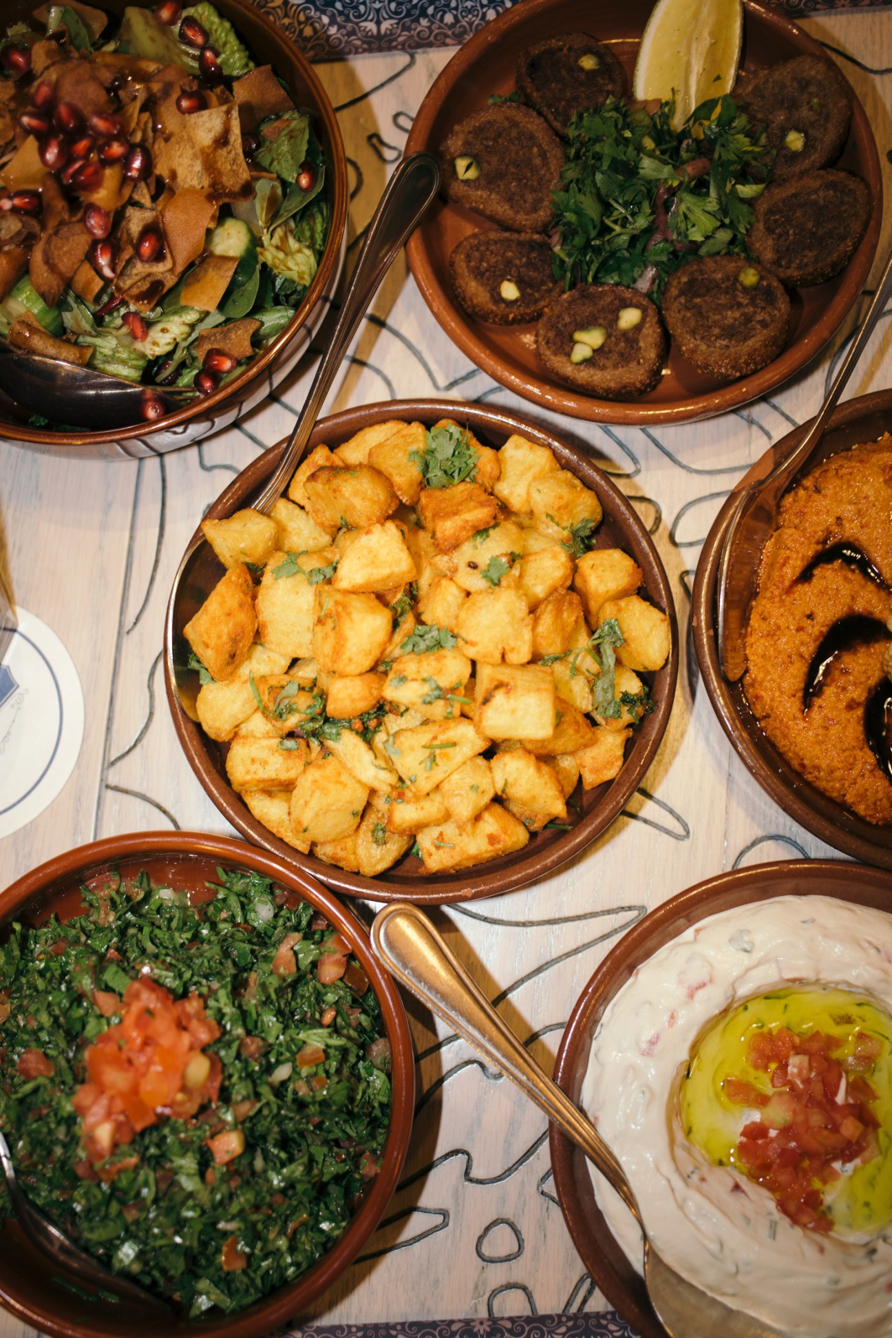 Overhead view of Lebanese mezze dishes at Loris restaurant including fattoush, coriander potatoes, tabbouleh and hummus in terracotta bowls.