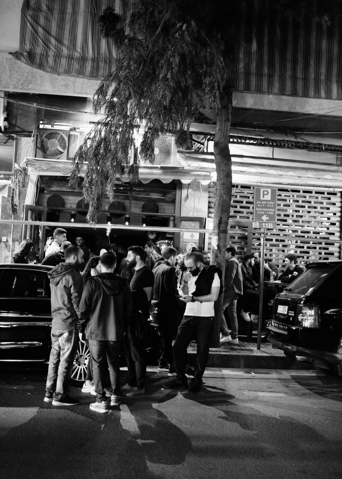 A group of people gathered on a Beirut street outside a bar in the Mar Mikhael neighborhood at night.