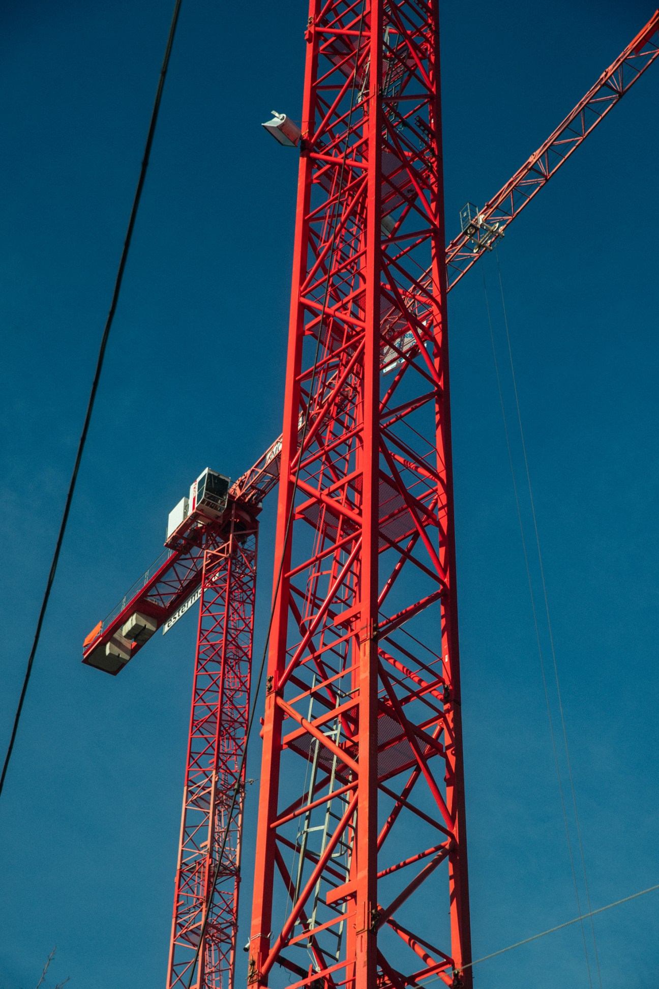 Red construction cranes towering against a clear blue sky