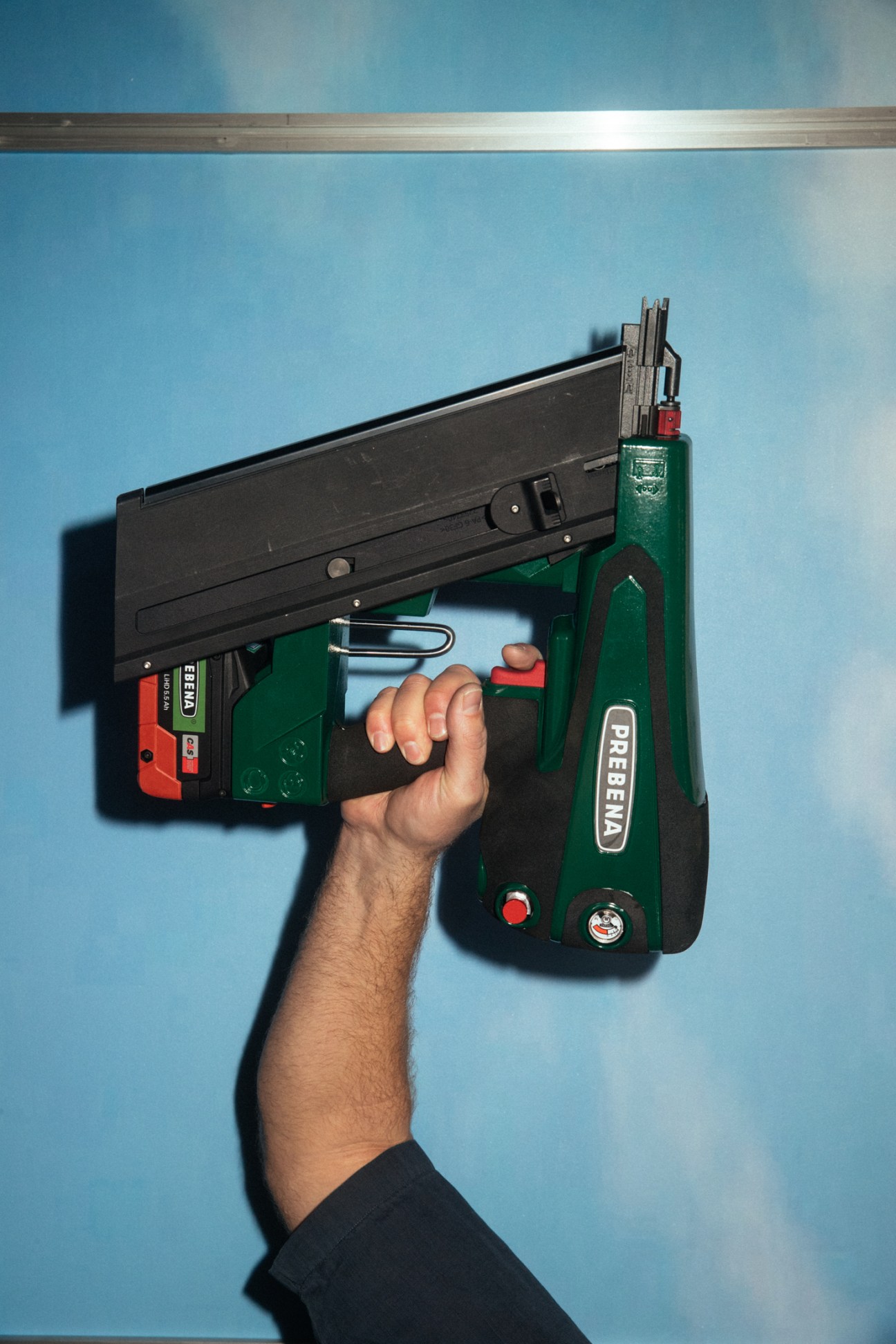 Hand holding Prebena's green cordless nailer against blue wall