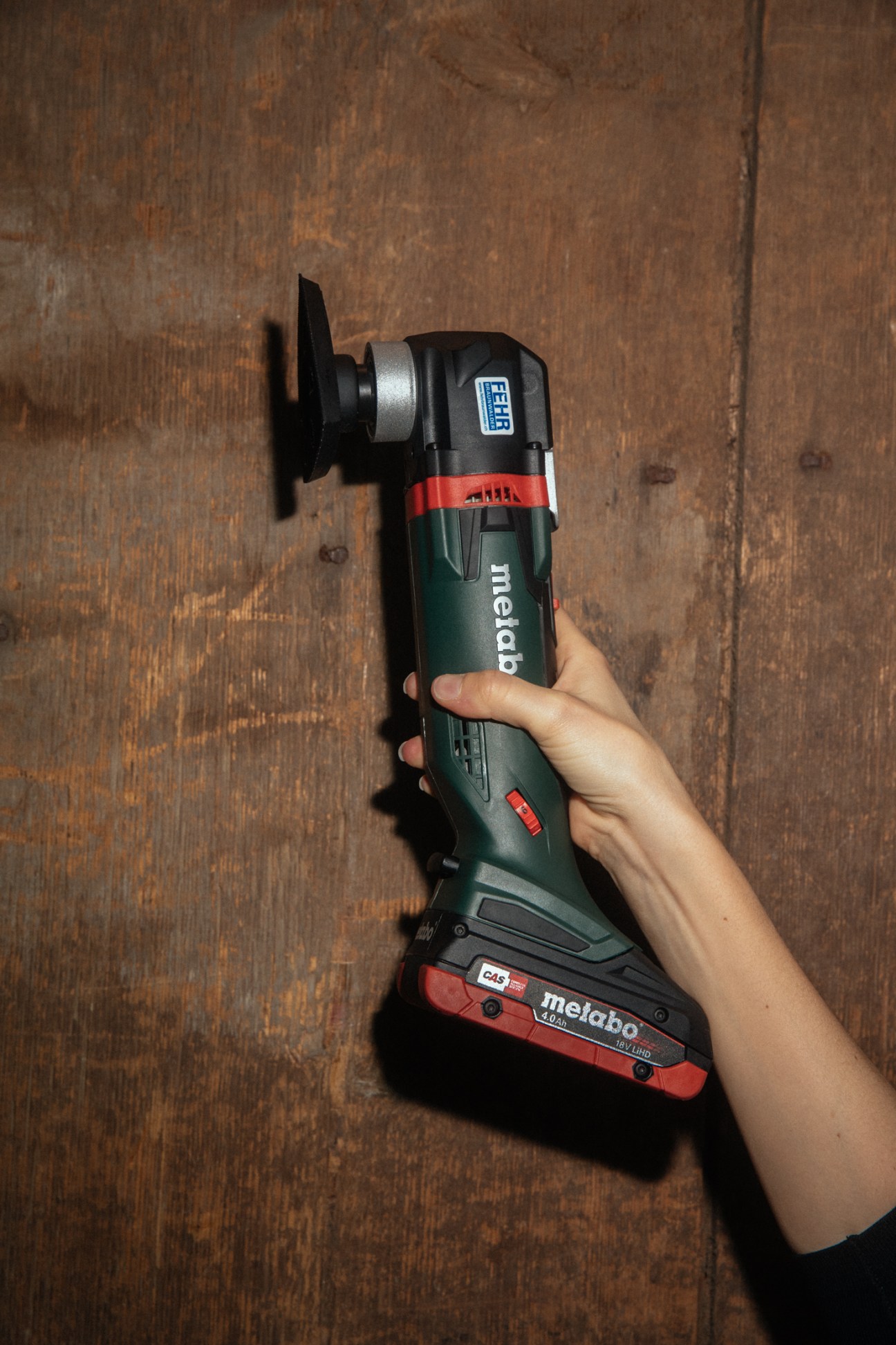 Hand holding a green and black Metabo cordless power tool with battery pack attached