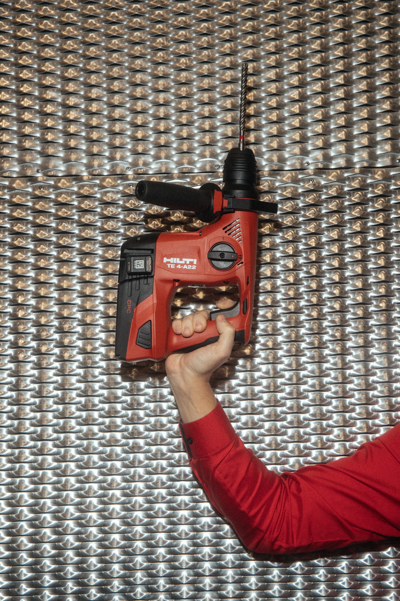 Hand holding red Hilti cordless drill against geometric metallic backdrop
