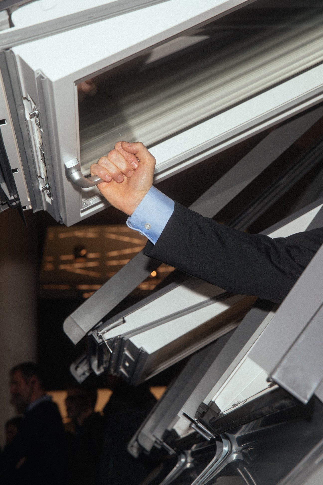 Hand in dark suit with blue cuffed shirt gripping handle of open white Velux roof window