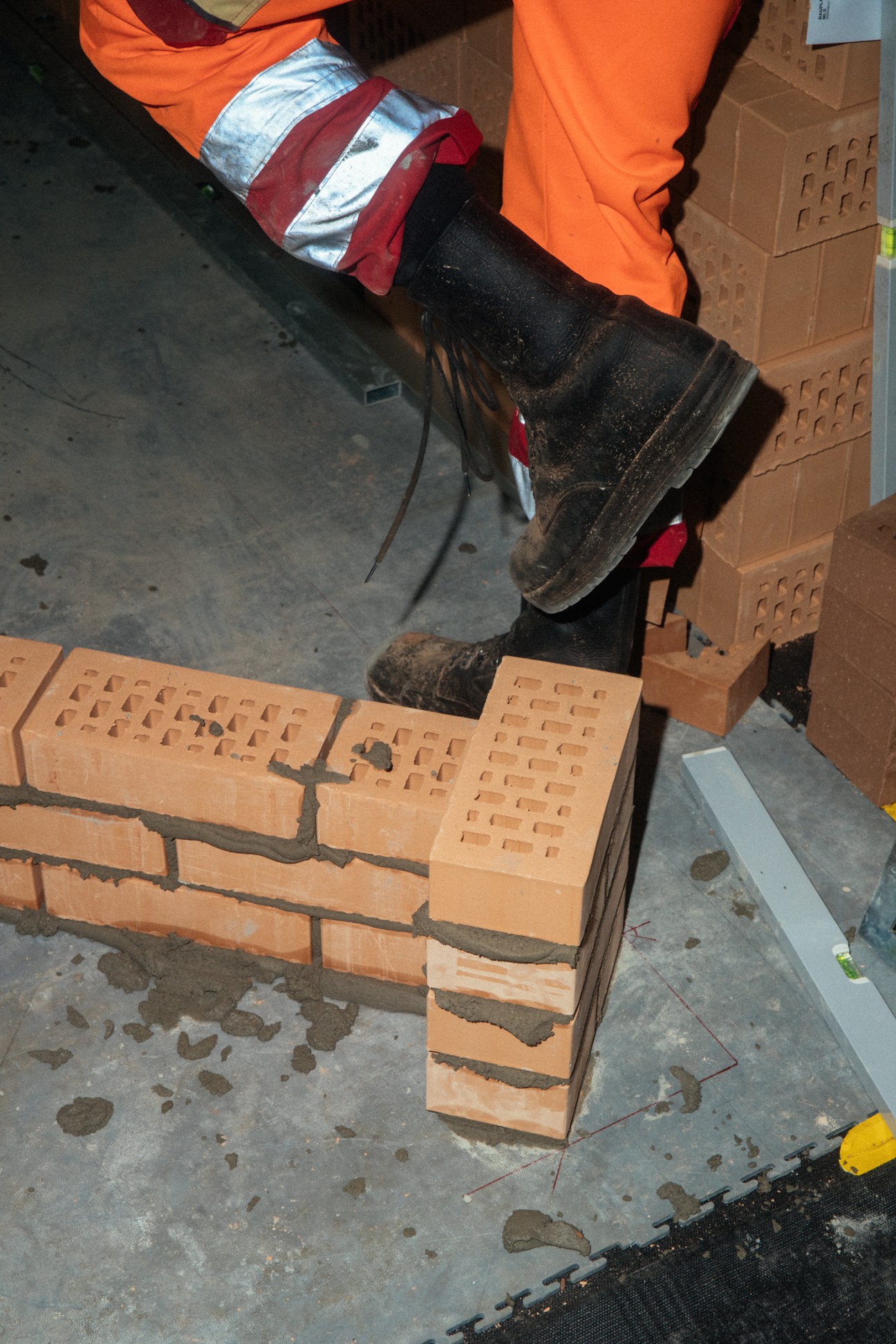 Construction worker in orange safety gear and black boots laying perforated bricks during bricklaying competition