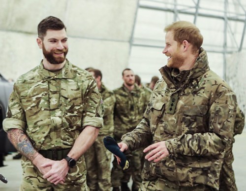 Two bearded men in camouflage military uniforms standing together outdoors.