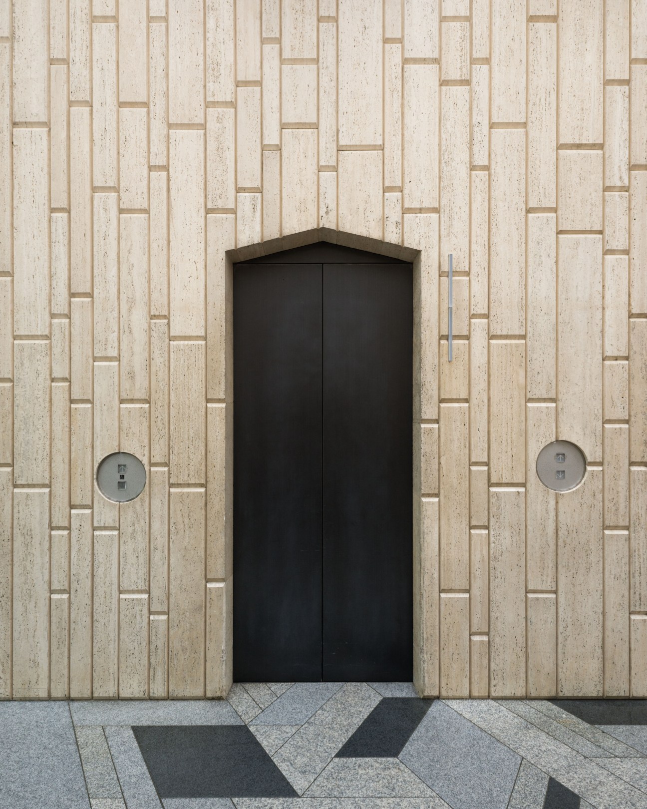 Travertine and marble lobby entrance of 114 Bank with geometric patterned flooring and black doors.