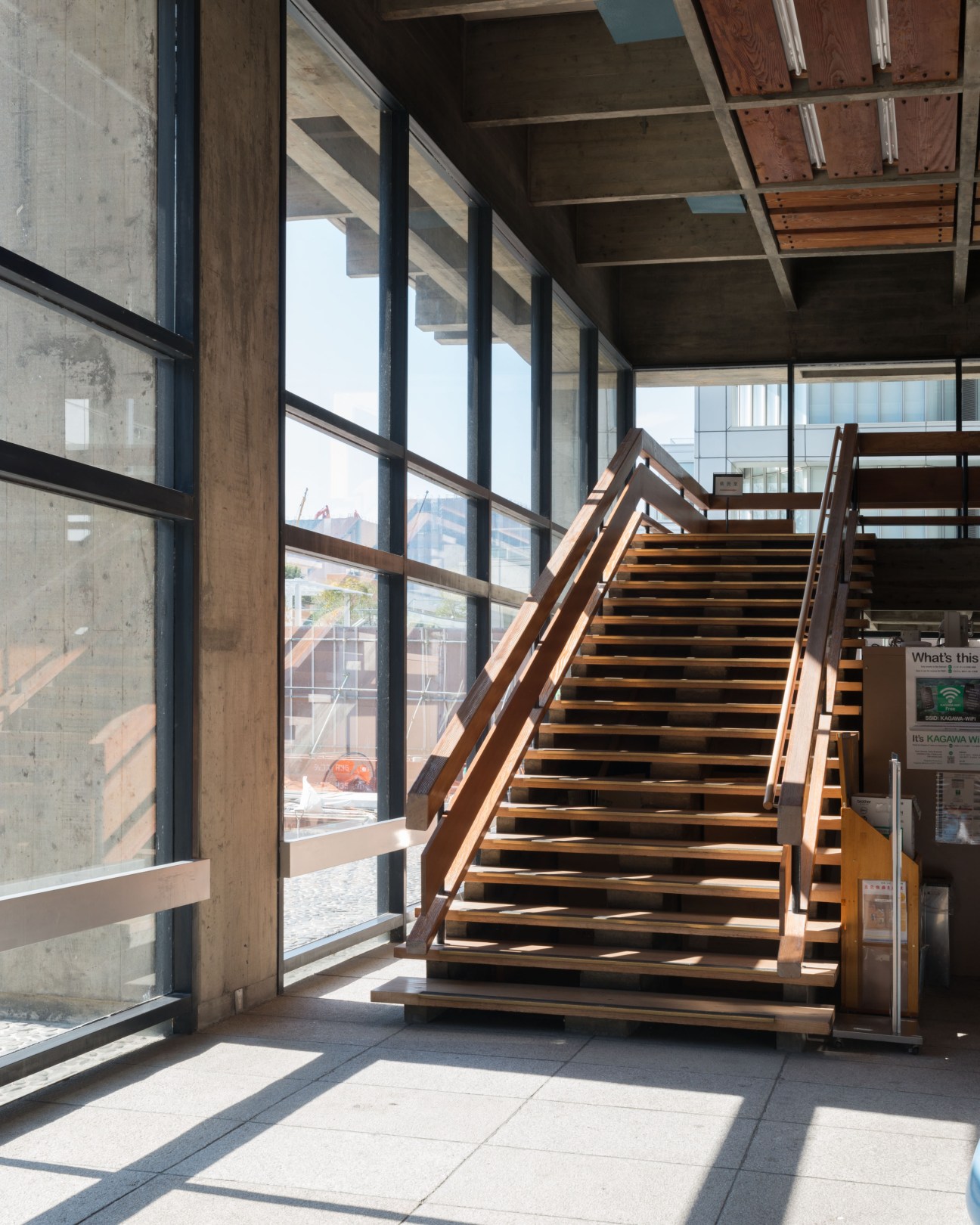 Interior view of Kagawa prefectural office foyer with wooden staircase and concrete brutalist architecture.