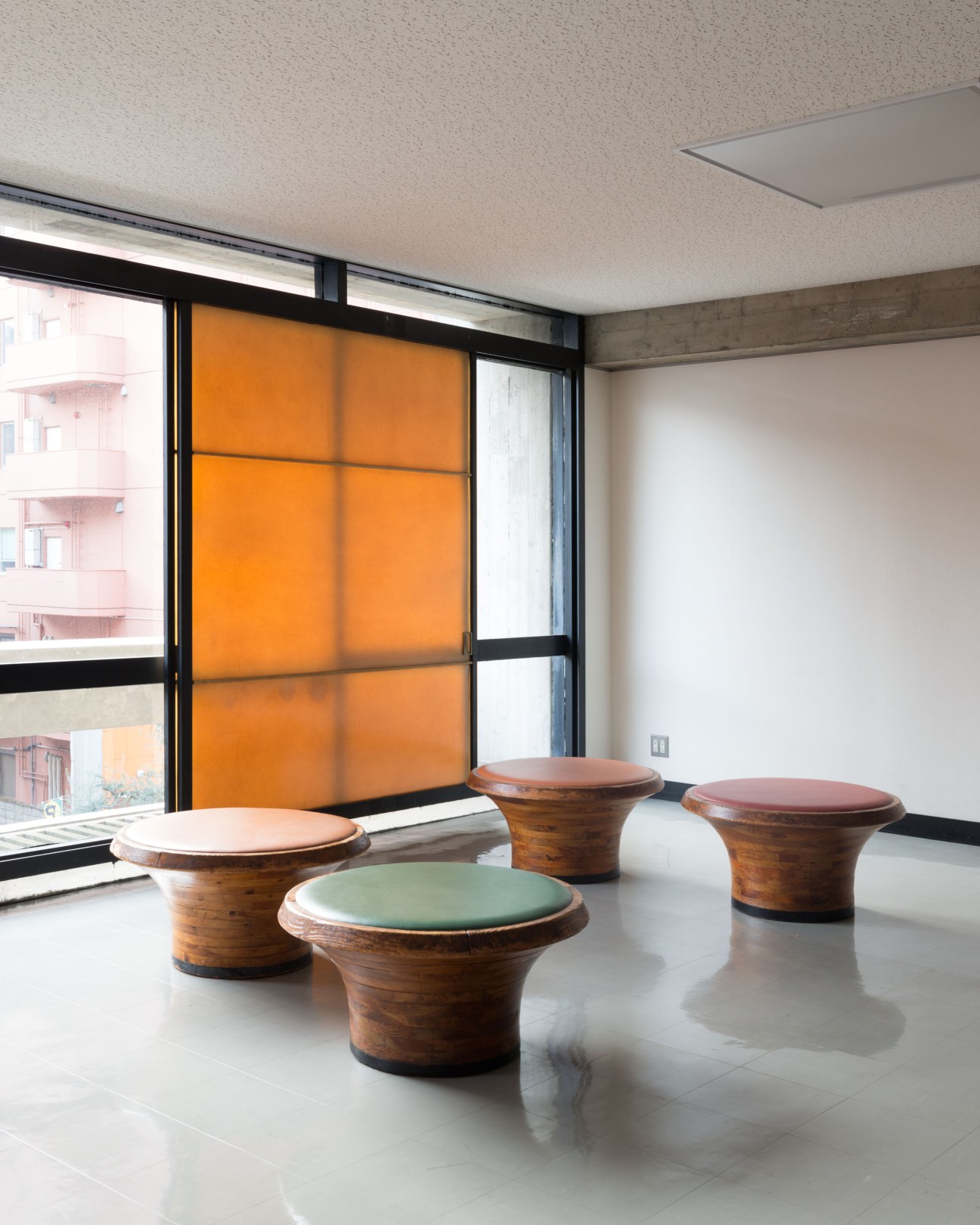 Wooden stools with colored cushions in a modernist interior with orange-tinted windows.