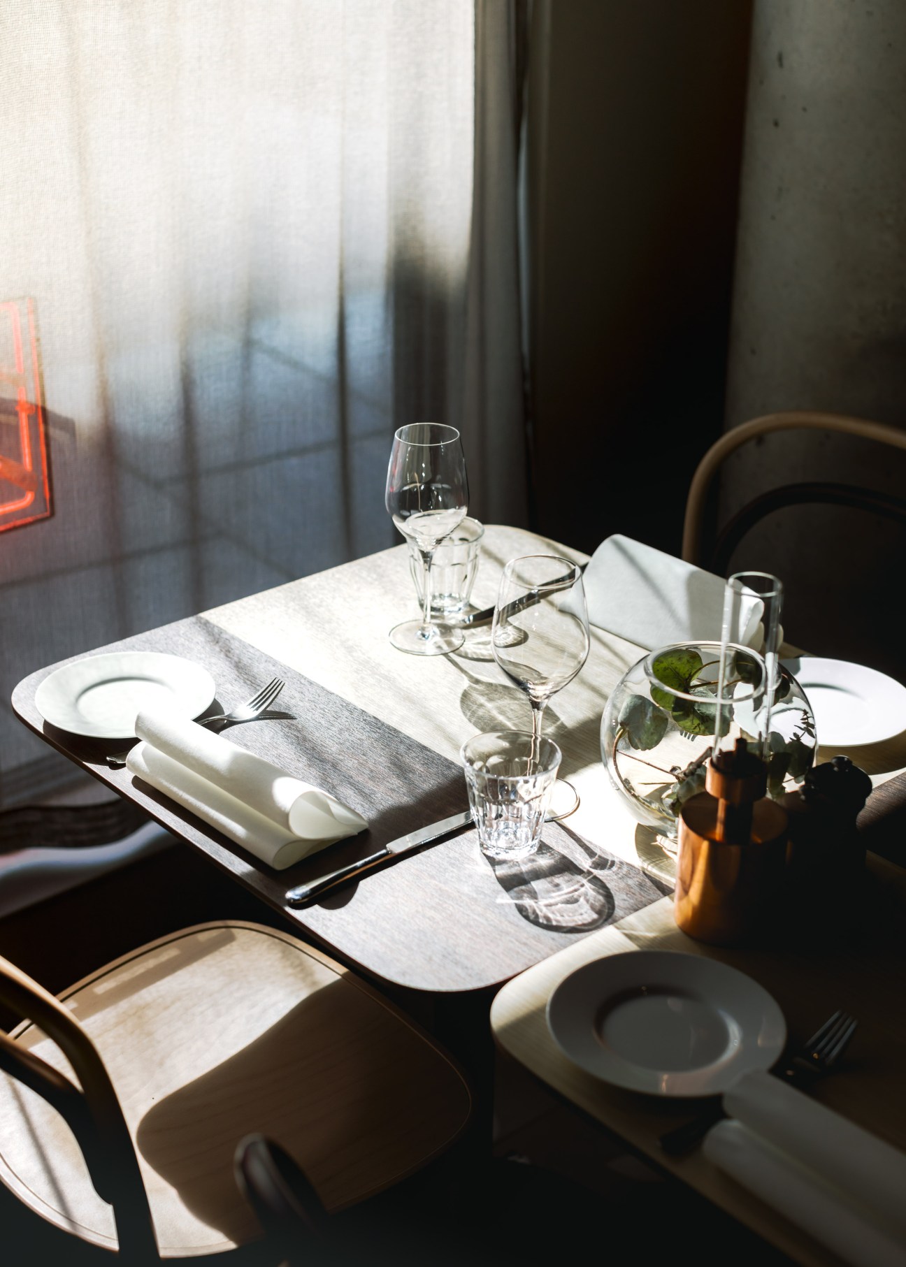 A minimalist dining table set with white plates, wine glasses, and a grey linen napkin at Zander K hotel in Bergen.