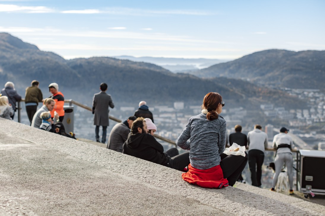 Tourists and locals enjoying the view from Mount Fløyen overlooking Bergen's mountains, fjords, and city below.