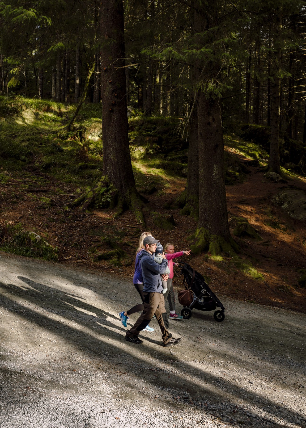 Woman jogging with child and stroller on forest path in Bergen, Norway.