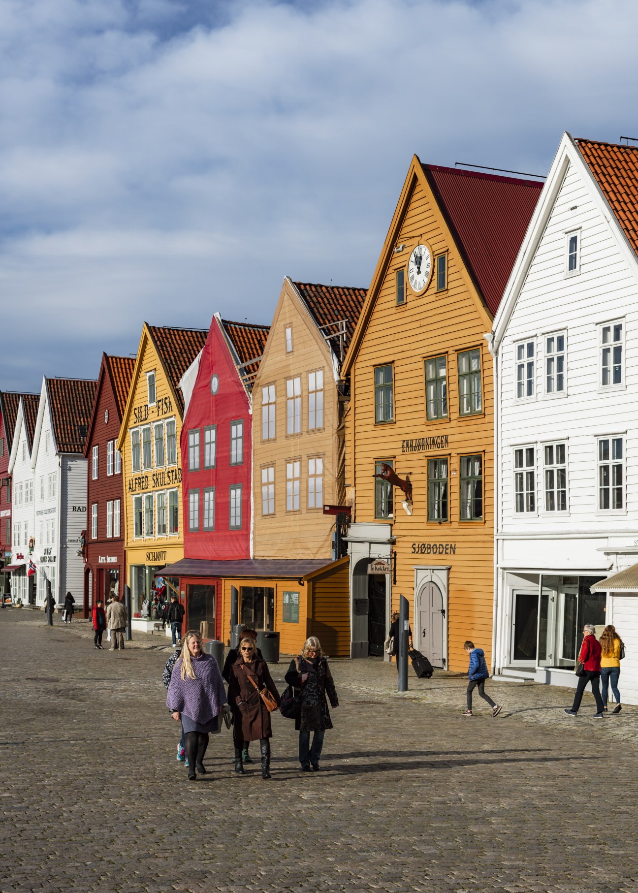 Colourful wooden buildings with terracotta roofs in Bergen's Vågen harbour with pedestrians in the square.