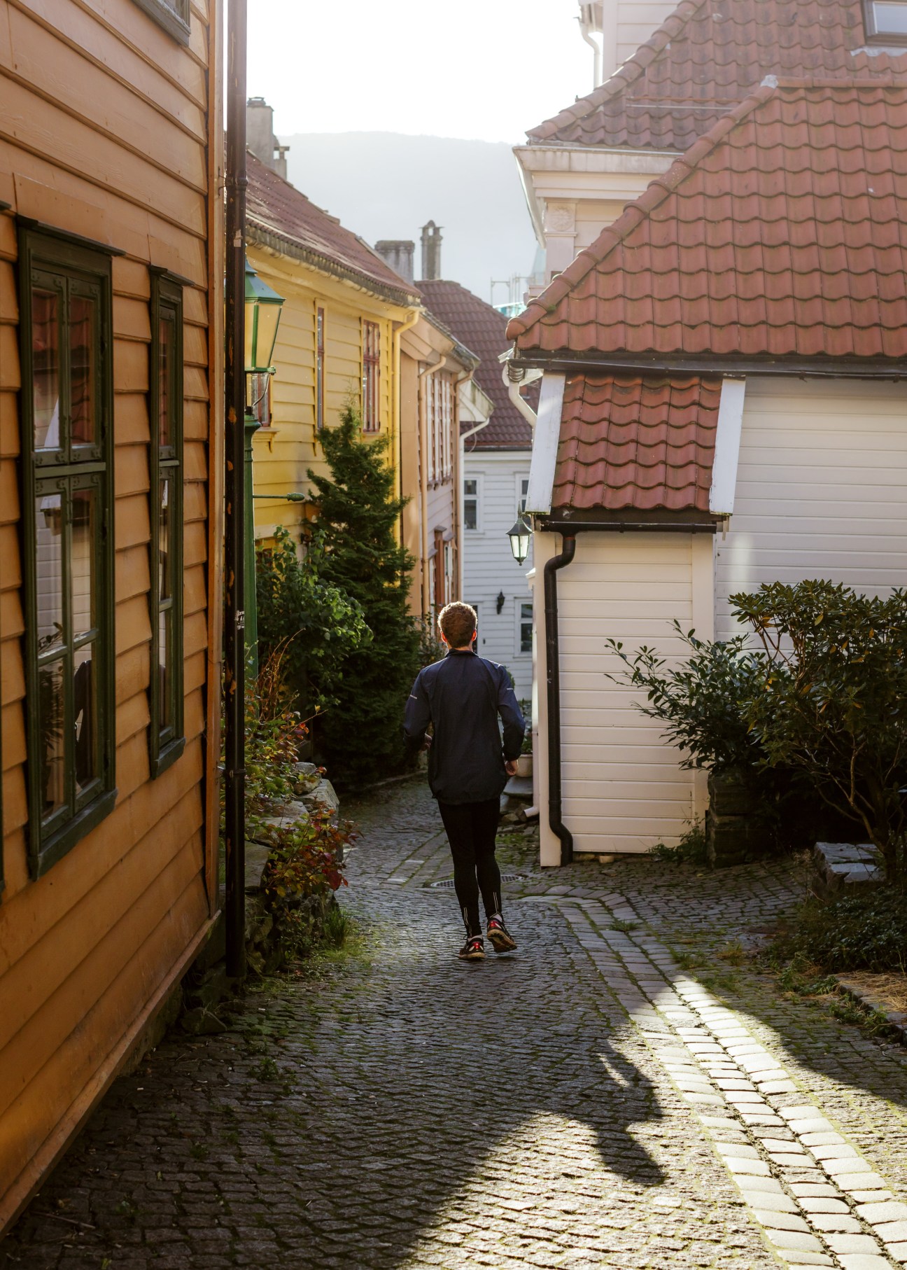 A jogger runs through a narrow cobblestone alley lined with colorful wooden buildings in Bergen, Norway.