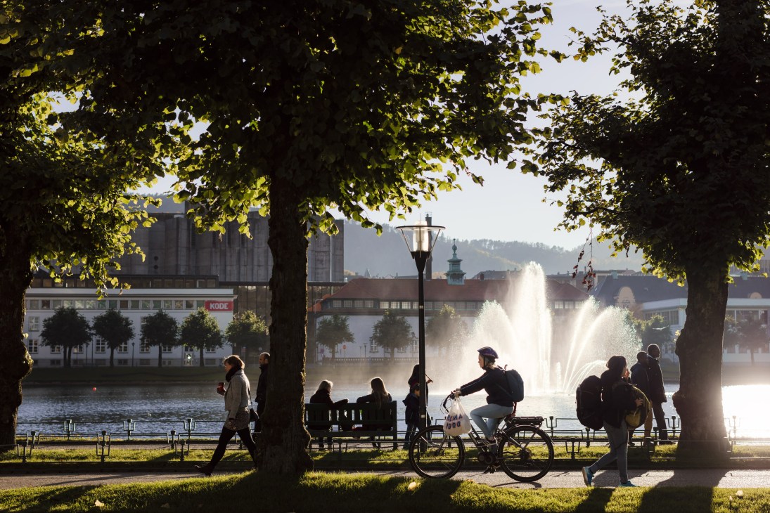 People relaxing by fountains at Lille Lungegårdsvannet lake in Bergen city centre under tree canopy.