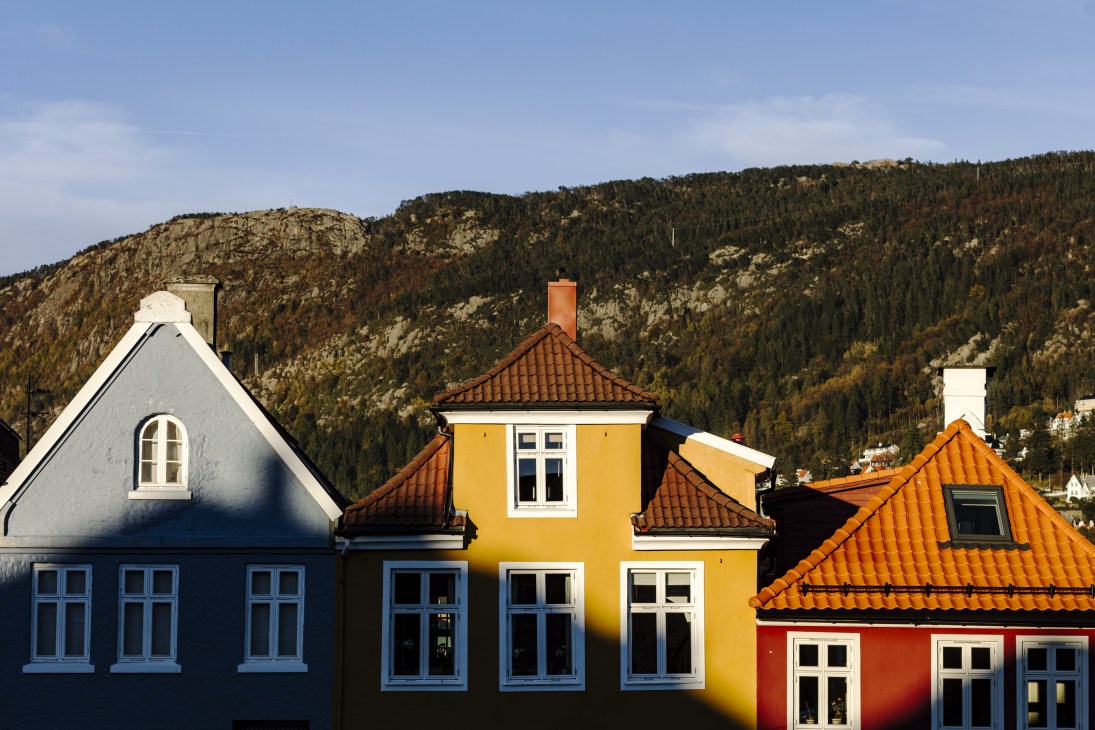 Colorful wooden houses with pitched roofs against forested mountains in Bergen's Nordnes area.