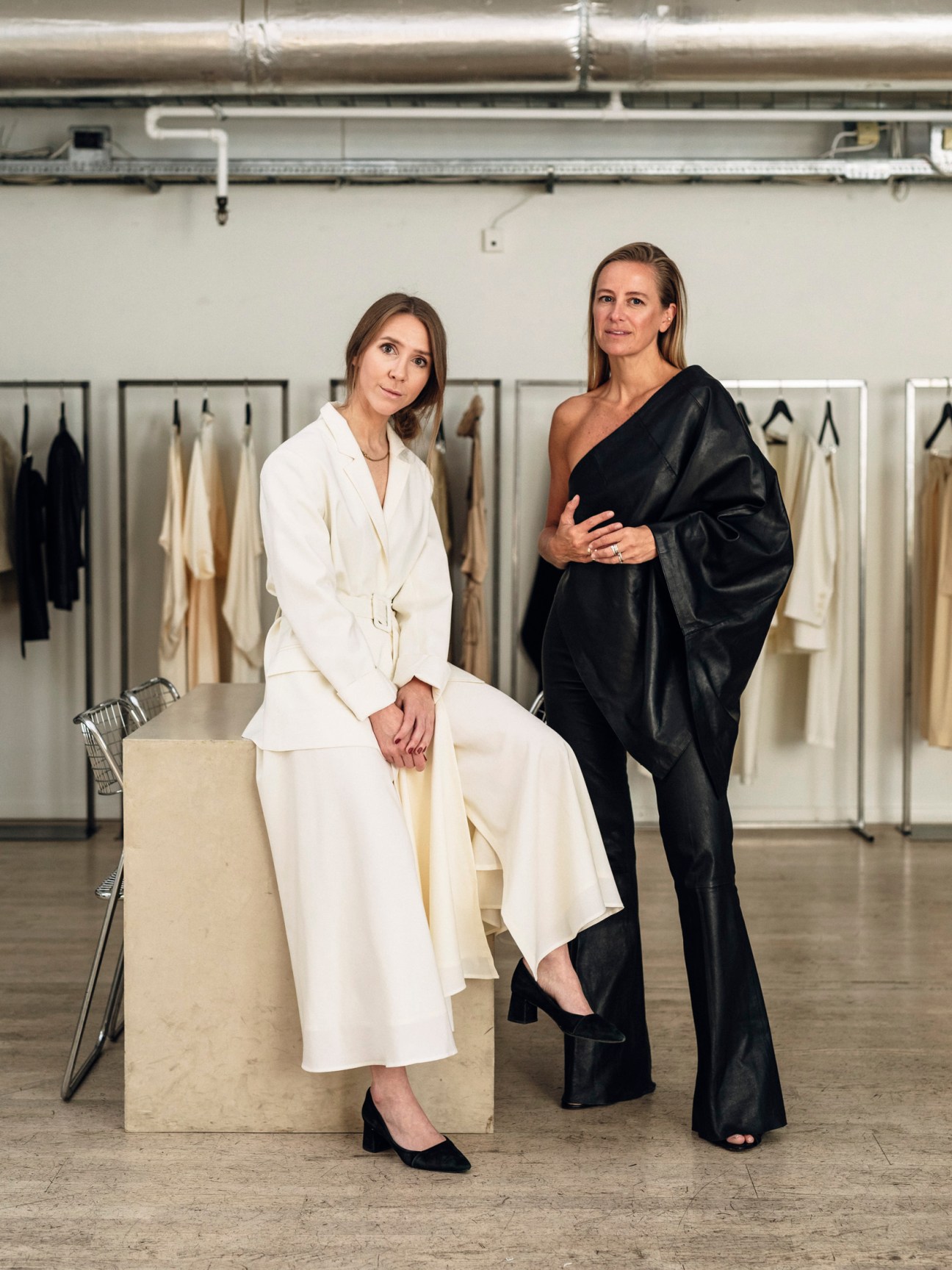 Pia Nordskaug and Celine Aagaard, co-founders of Envelope 1976, pose in their studio with clothing racks behind them.