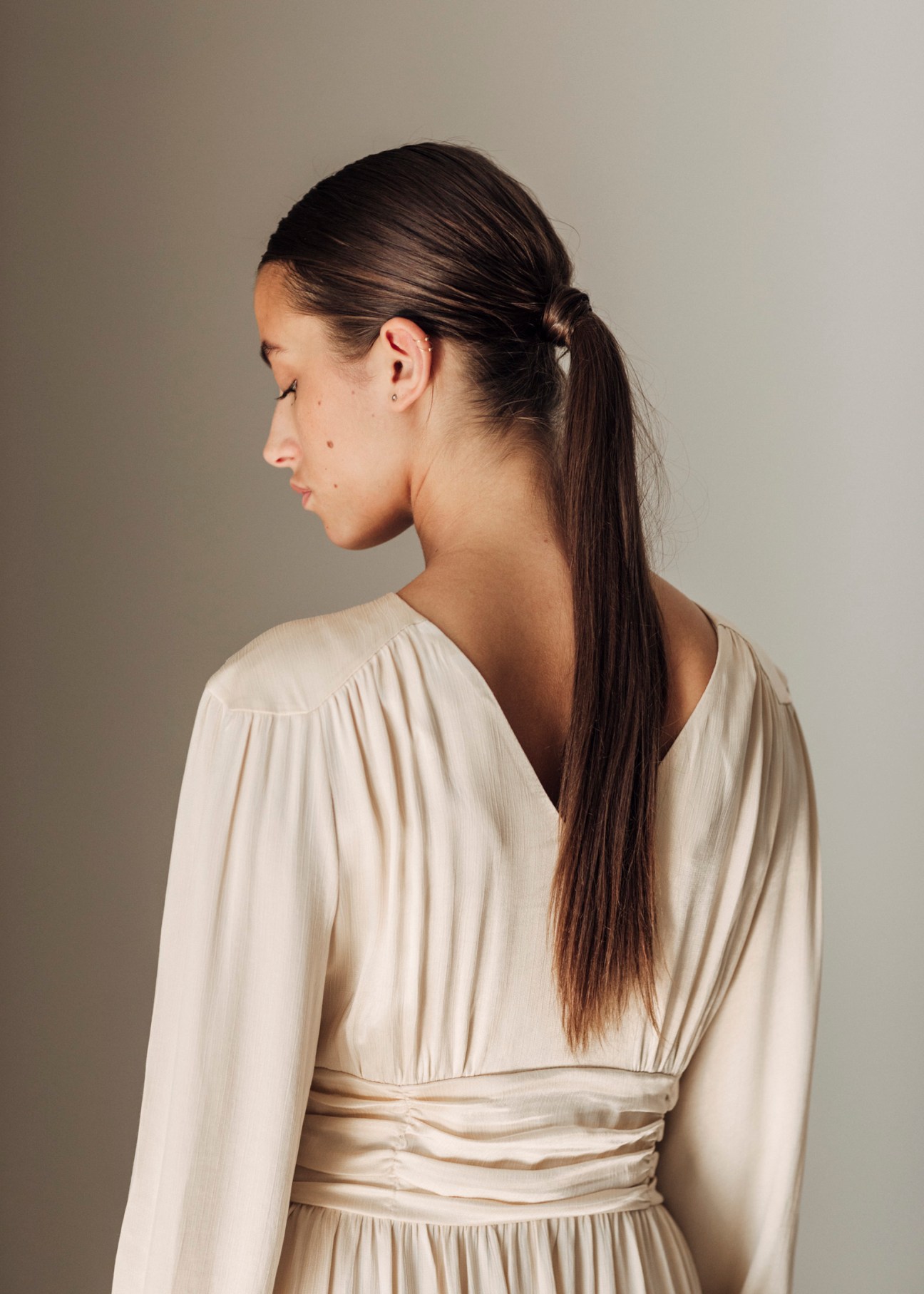 Woman wearing Envelope 1976's cream Sitges dress with gathered waist, shown in profile against neutral background.