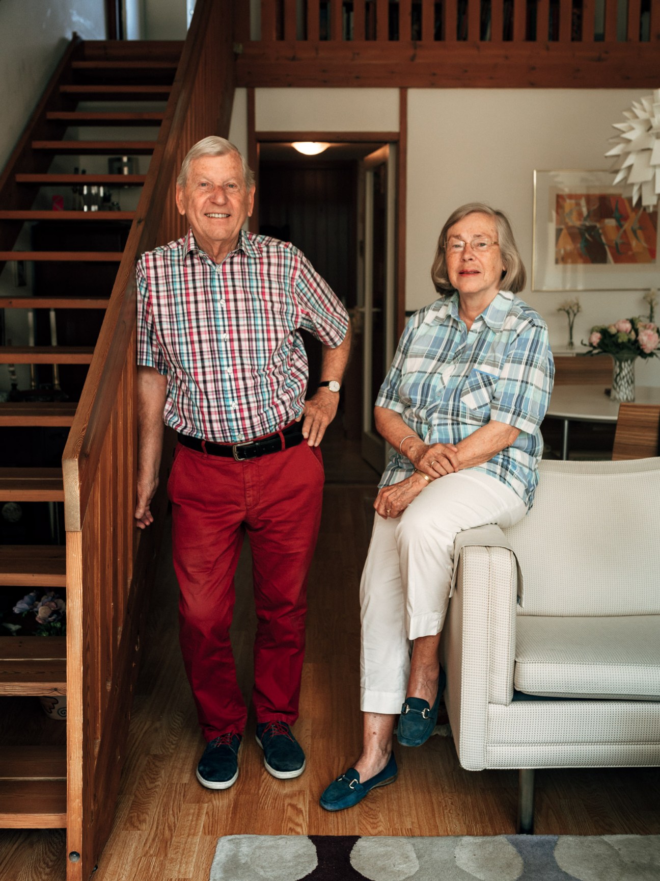 An older man and woman stand in a light-filled interior with wooden stairs and modern furnishings at the Fredensborg Houses.