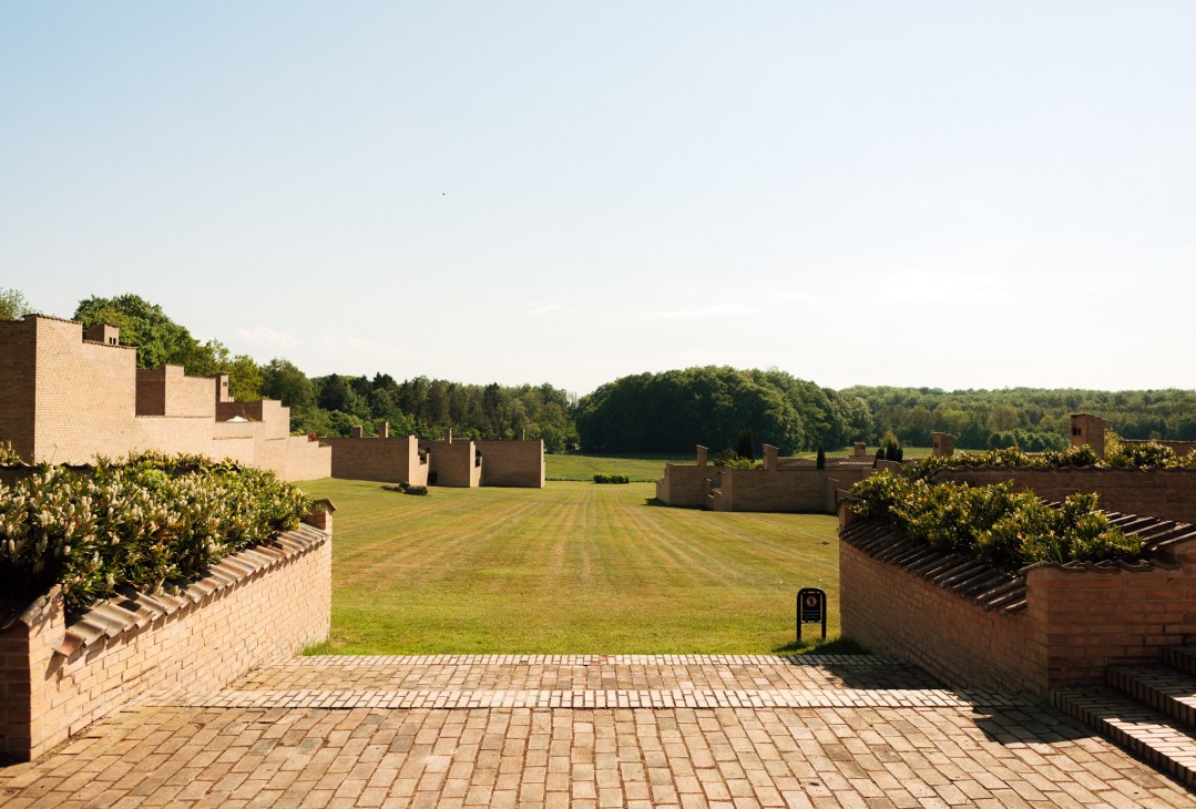 A large courtyard garden at Jørn Utzon's Fredensborg Houses with manicured lawn, brick walls, and forested hills beyond.