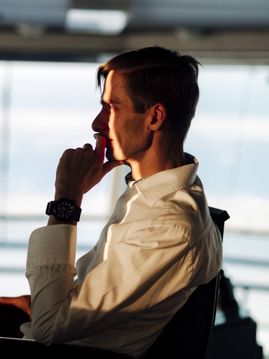 First officer Miikka Ylikoski in profile aboard the icebreaker Kontio, wearing a cream shirt and black watch, gazing out at the frozen sea at dawn.