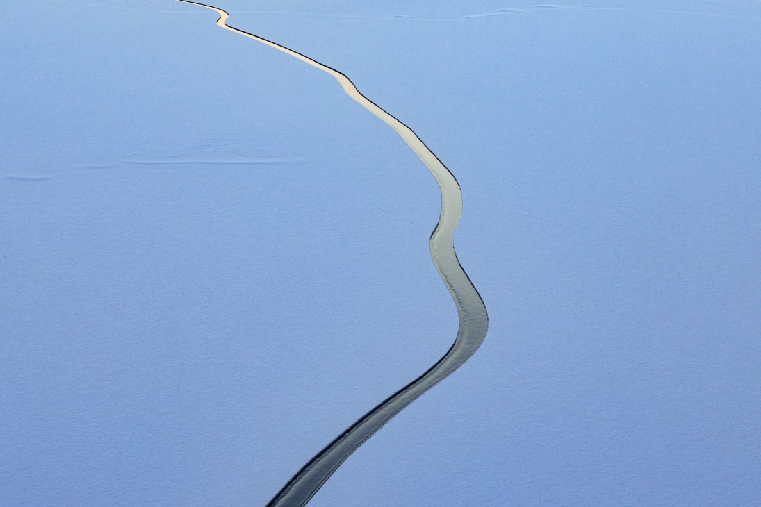 Aerial view of a winding channel cut through frozen sea ice, showing the contrast between the cleared path and surrounding white ice floes.