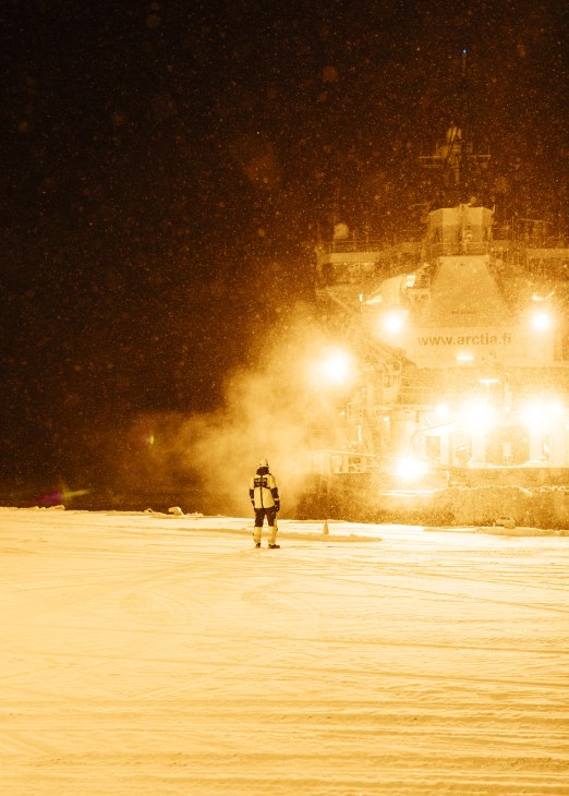 The icebreaker Kontio docked in the port of Oulu at night with bright floodlights illuminating the vessel and snow falling.