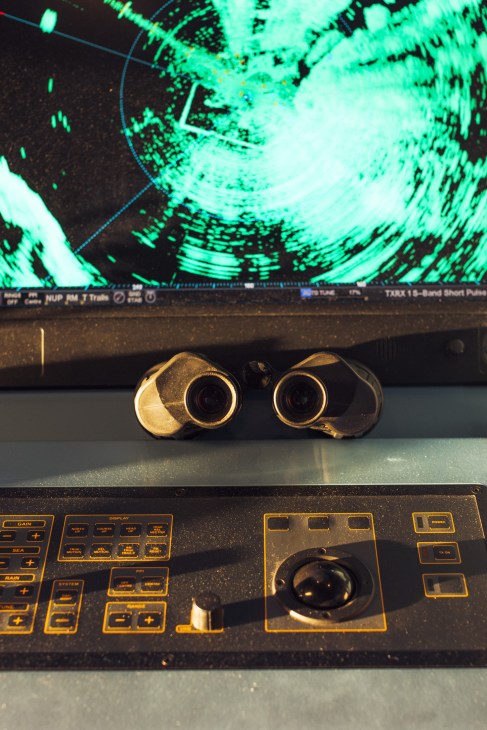 Radar screen displaying green sonar readout above icebreaker bridge control panel with brass binoculars.