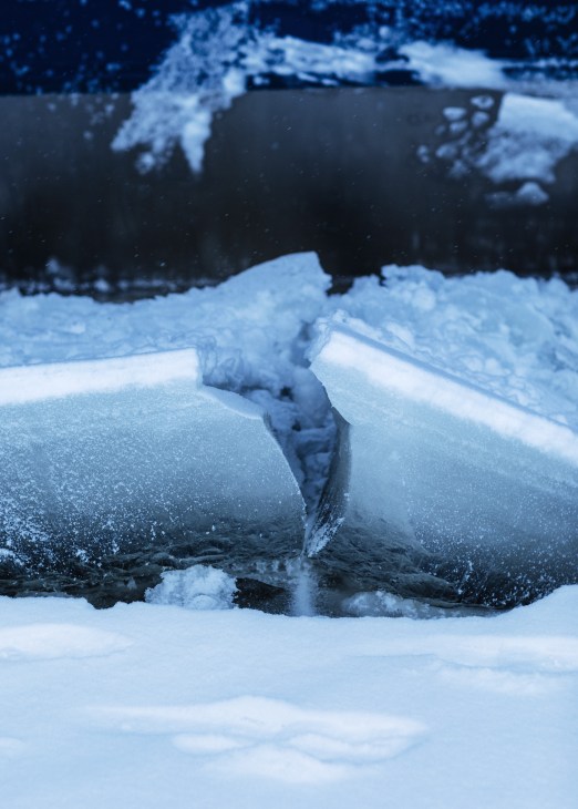 Thick ice fractured into chunky slabs by an icebreaker, with dark water visible in the cracks.