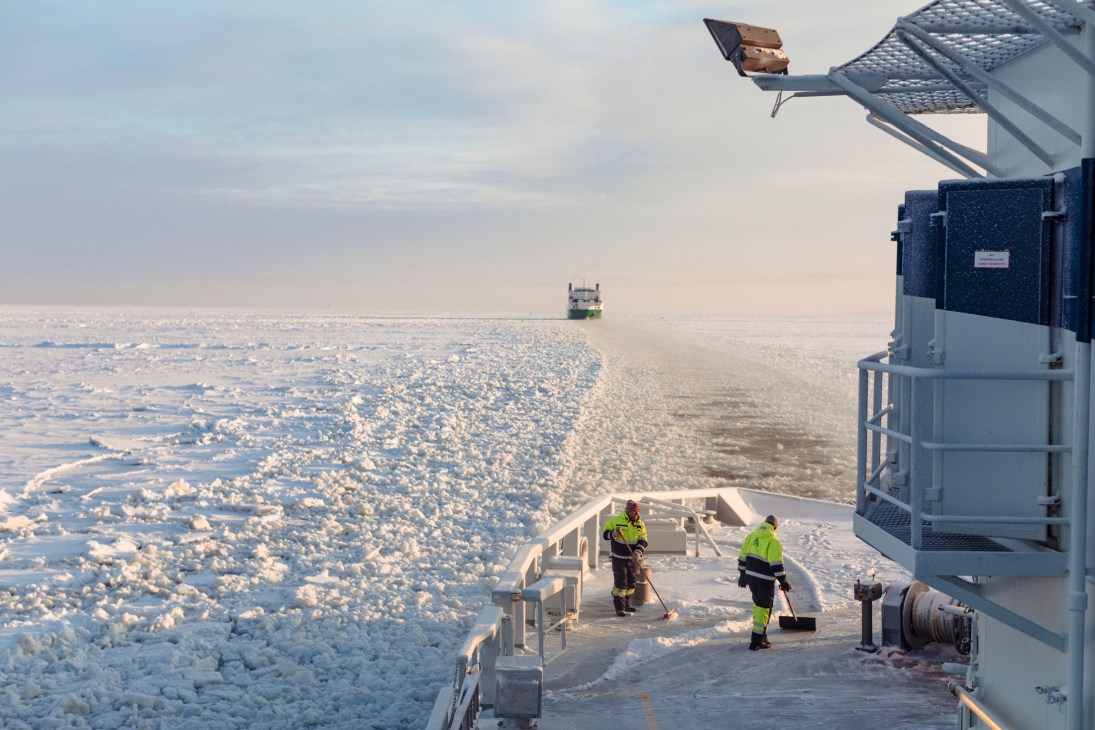 Two crew members in yellow safety gear clear ice from the deck of Finnish icebreaker Kontio in the Bay of Bothnia.