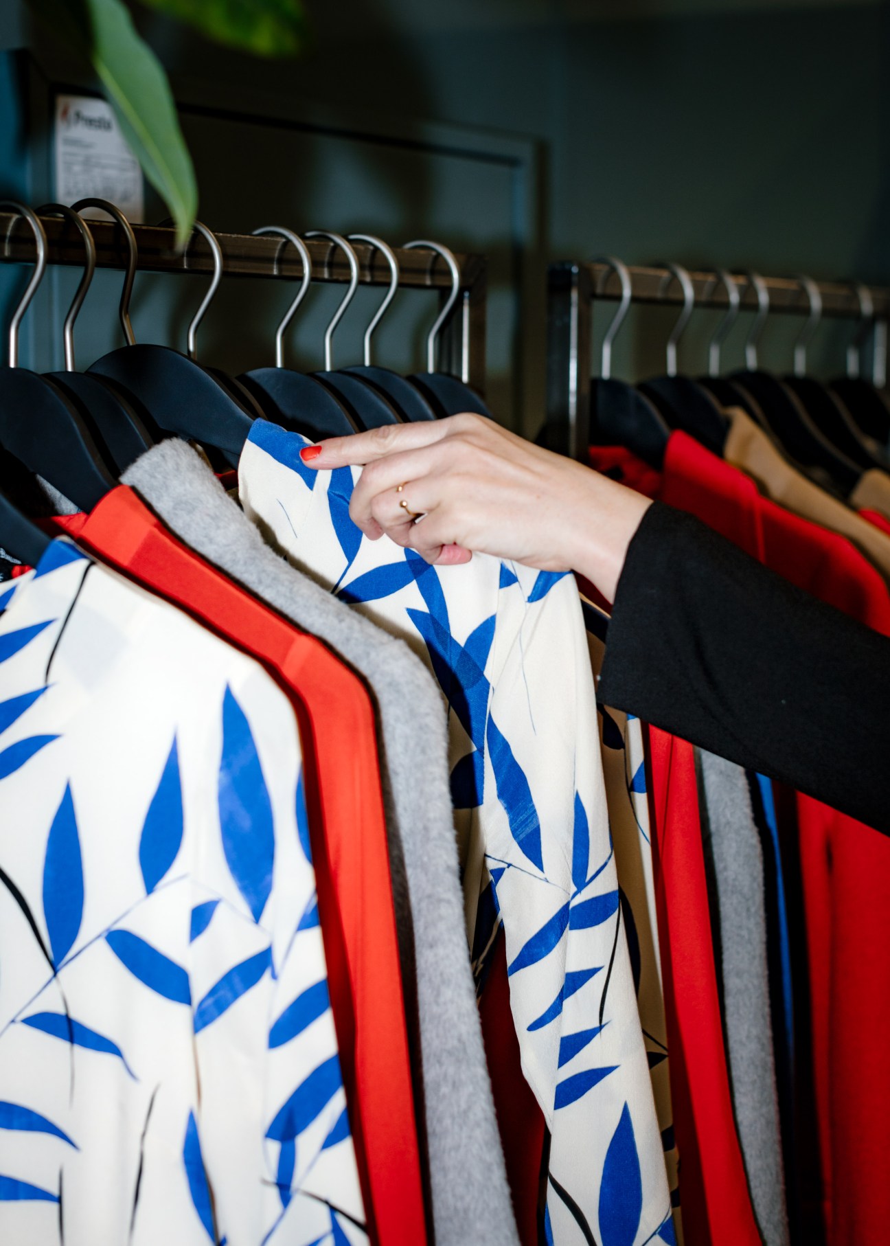 Hand touching a cream and blue patterned garment on a clothing rack with colorful designs.