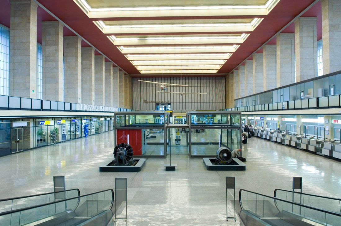 Spacious interior of Tempelhof airport's main foyer with art deco columns, skylights, and aircraft engines displayed.
