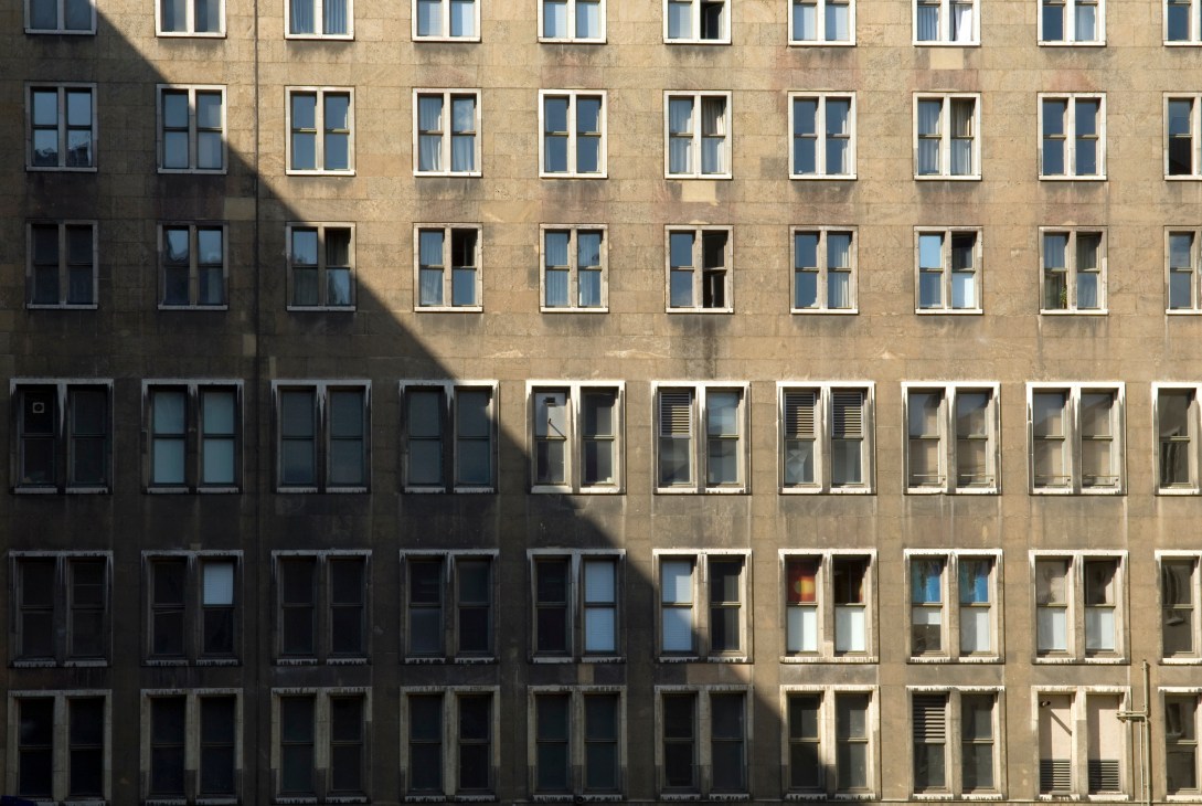 Exterior facade of Tempelhof airport building with regular grid of windows and shadow cast across stone wall.