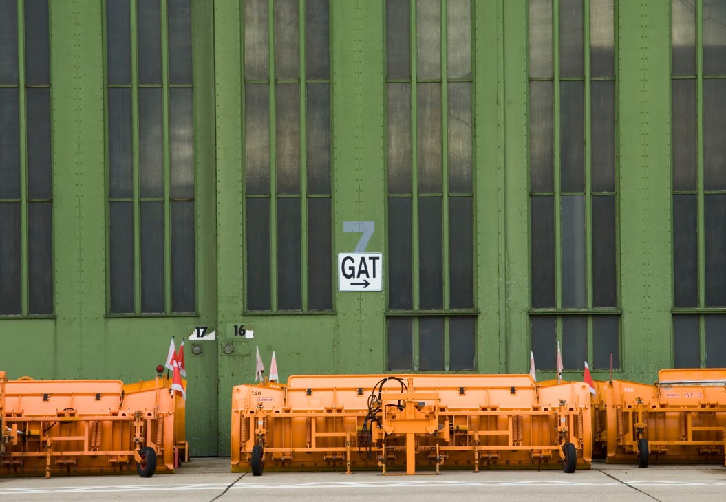 Orange airport ground equipment lined up against a green hangar wall with Gate 7 signage.