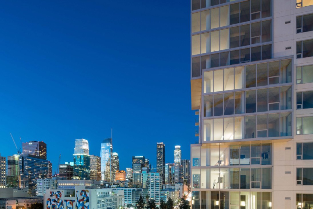 Modern residential high-rise building with illuminated windows at dusk overlooking a lit city skyline.