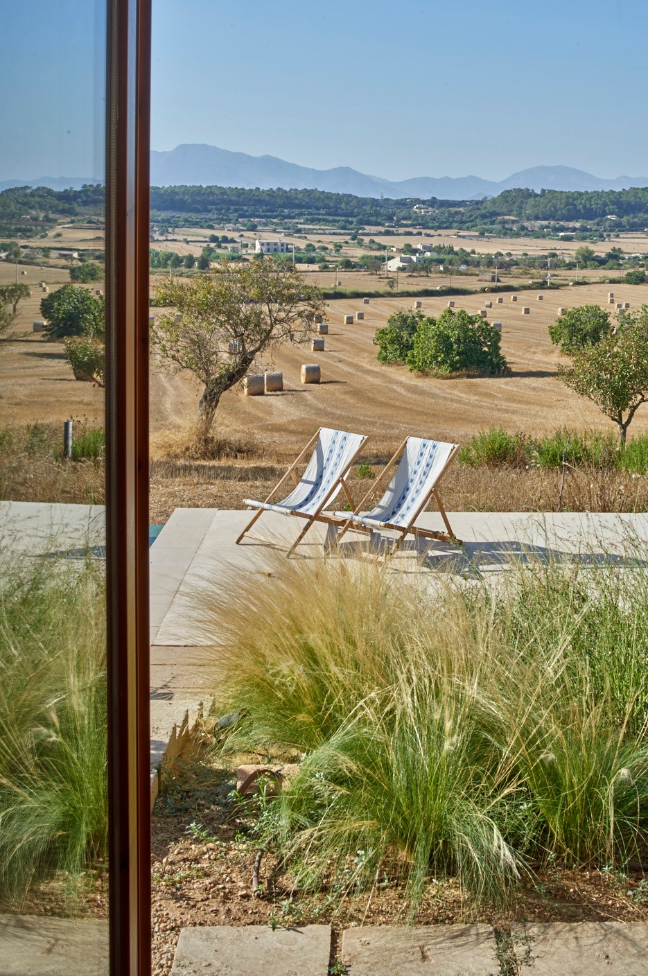 View through glass doors of terrace with two lounge chairs overlooking harvested fields and mountains