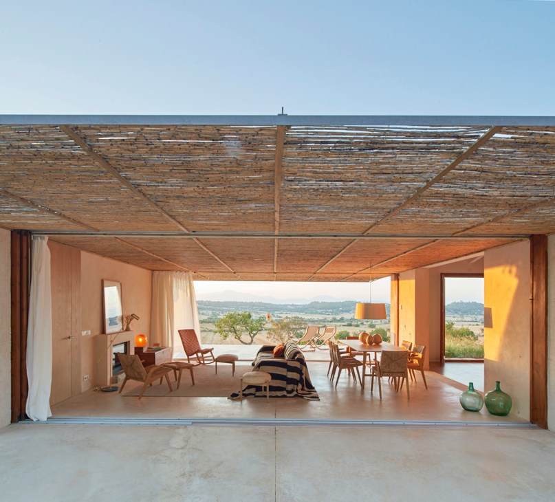 Modern living space with cane ceiling, leather furniture, dining area, and large opening to countryside view