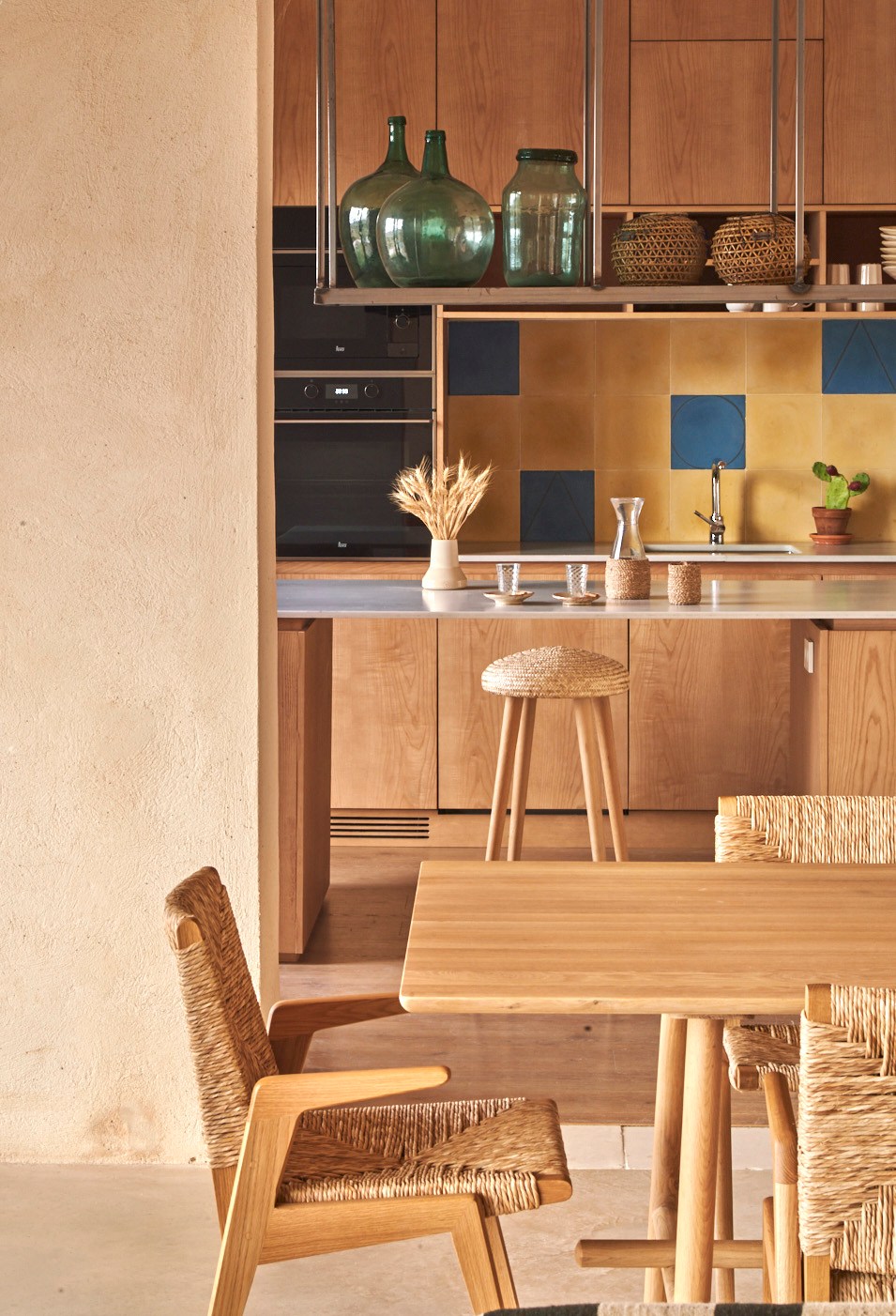 Kitchen with wood cabinets, colorful tile backsplash, woven bar stools and dining table