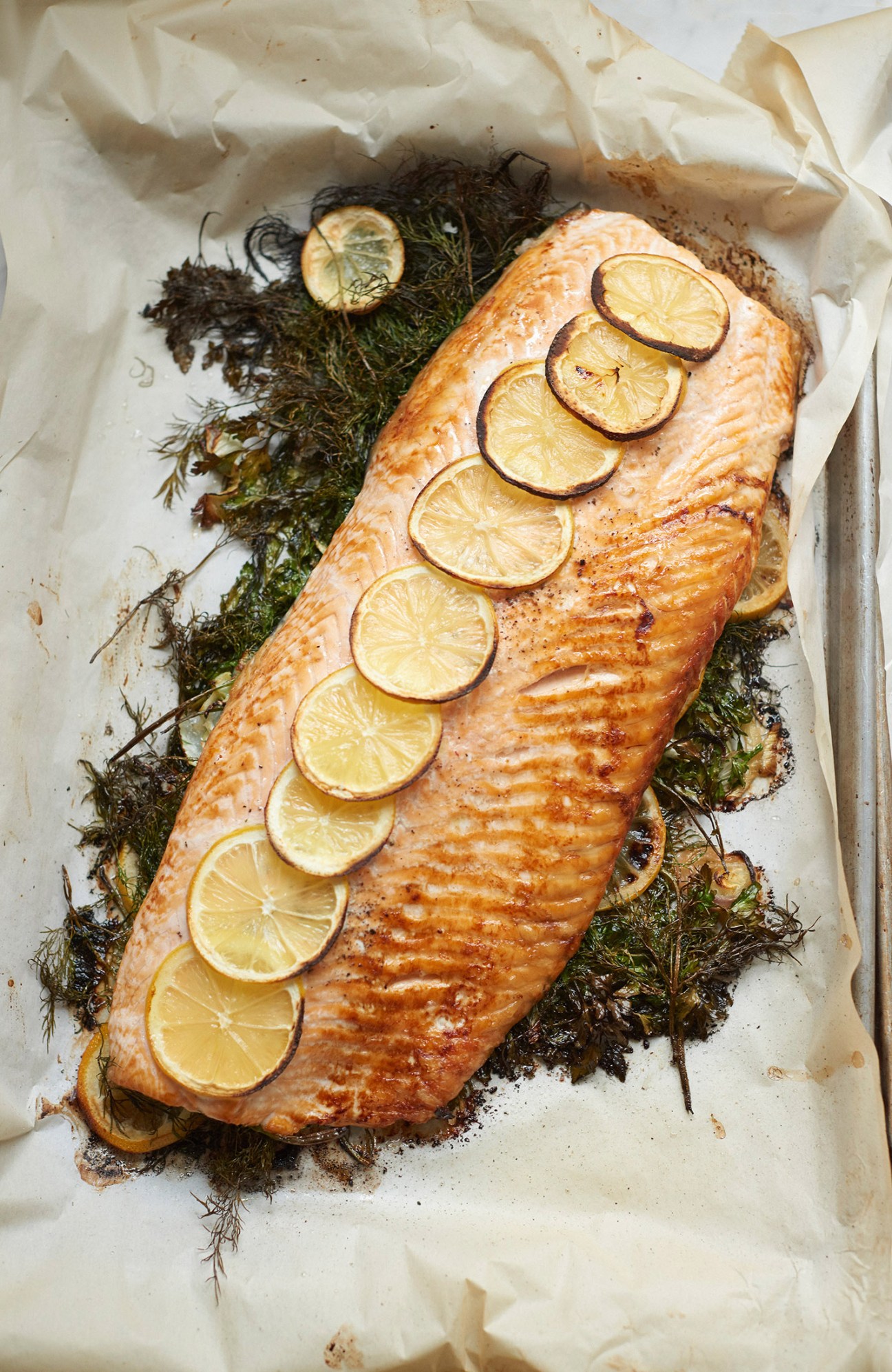 Roasted salmon fillet topped with lemon slices and fresh dill on parchment paper.