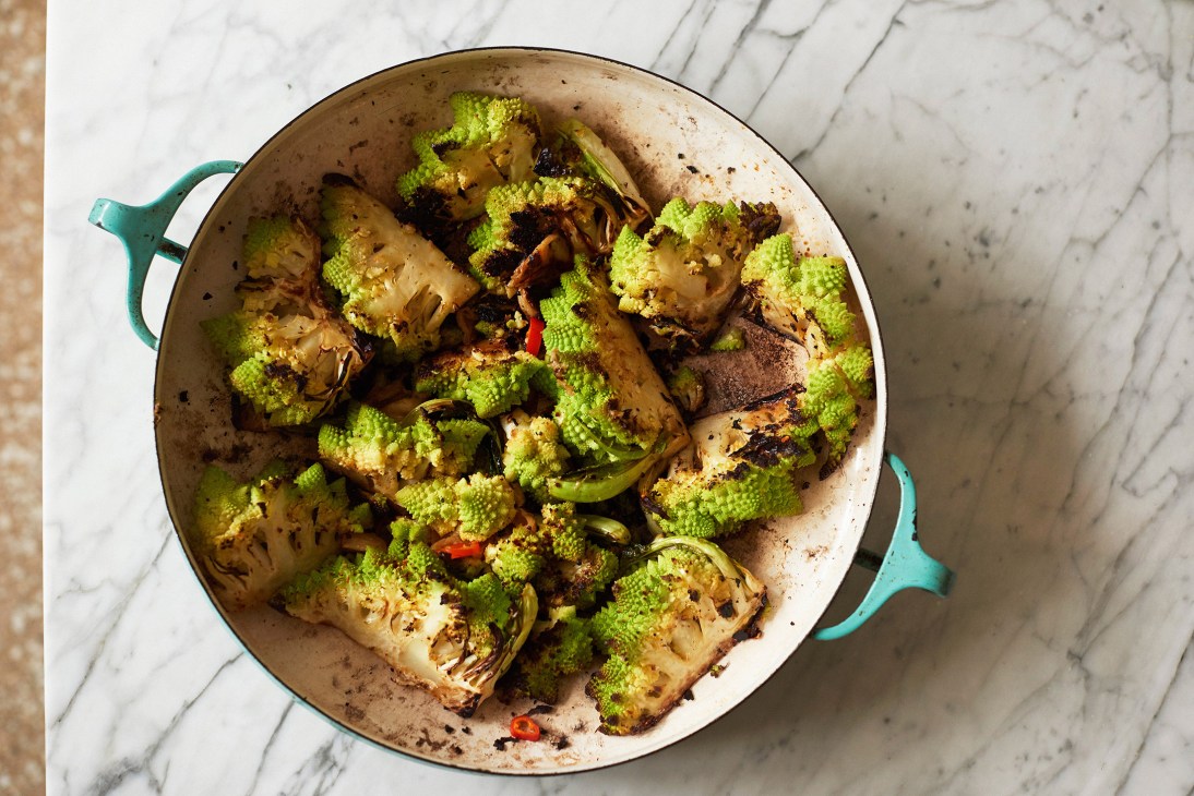 Roasted romanesco broccoli with confit garlic oil, aleppo pepper and lemon zest in a turquoise Dutch oven on marble surface.