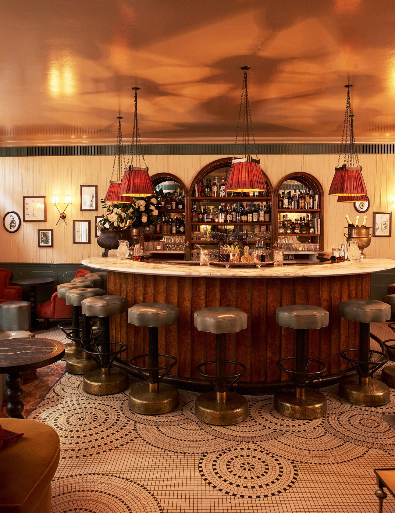 Kettner's horseshoe-shaped champagne bar with walnut counter, red pendant lamps, and arched backlit shelving.